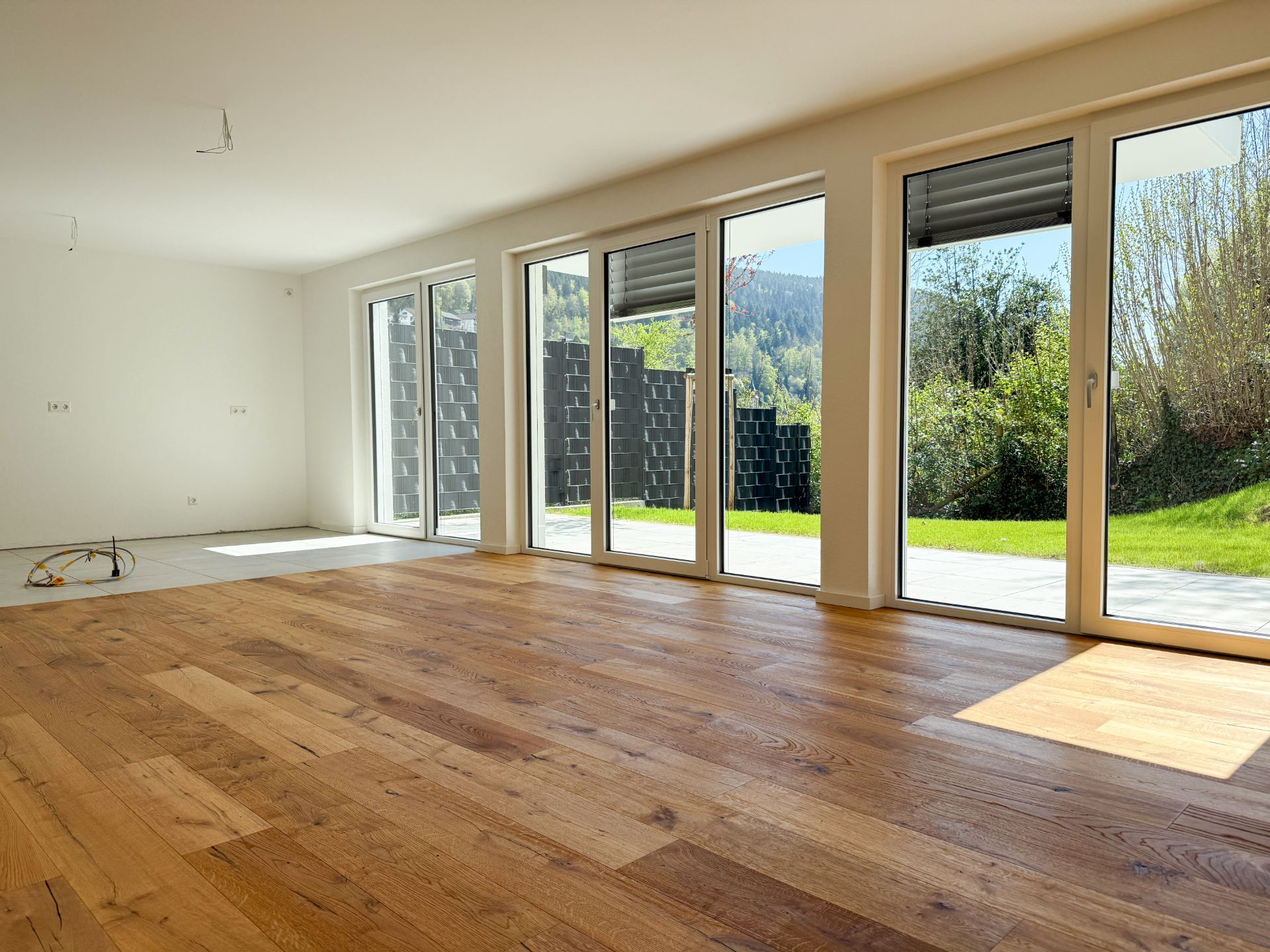 Helles Wohnzimmer mit Parkettboden und großen Fenstern mit Blick auf Garten und Terrasse.