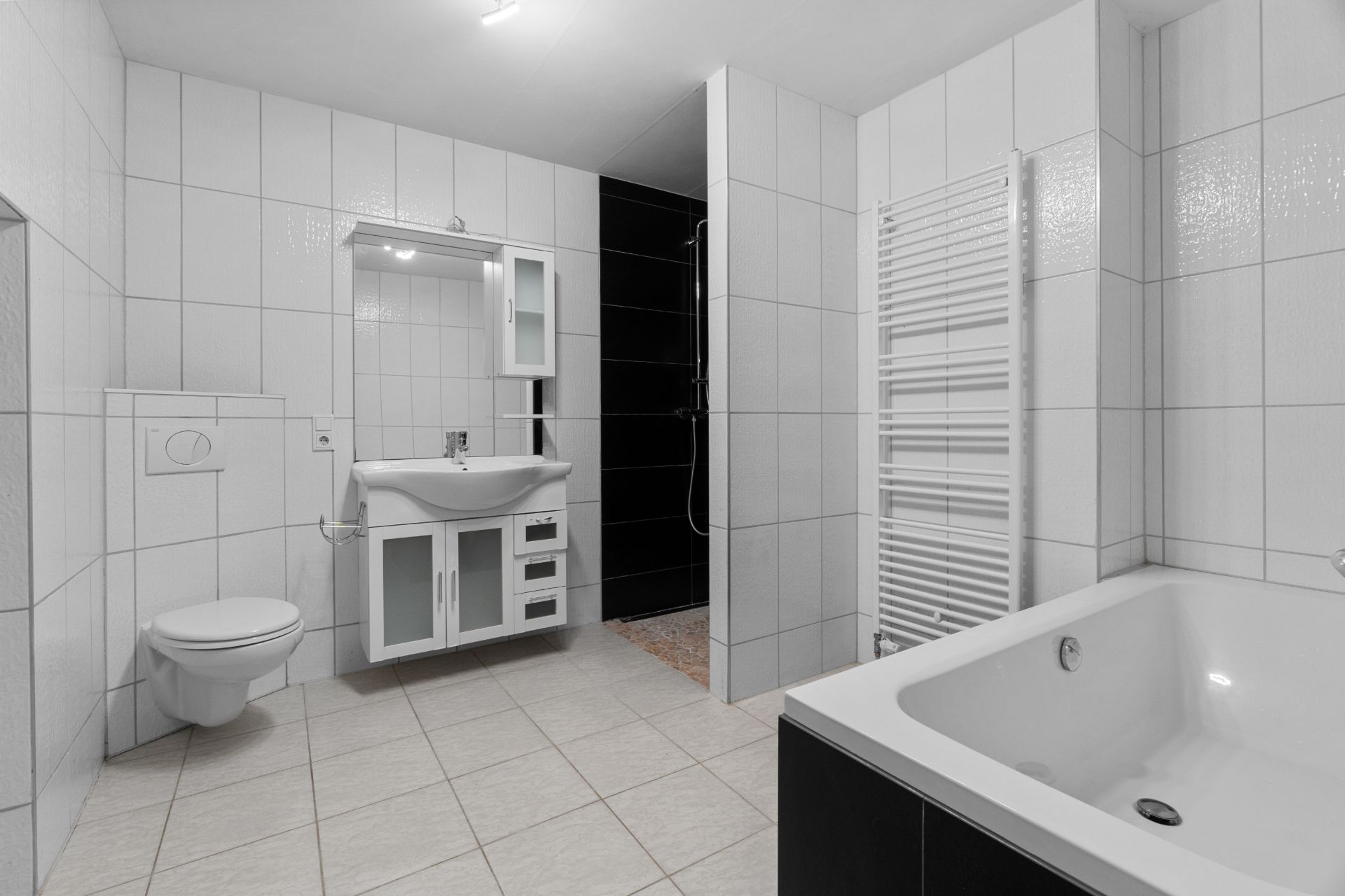 Modernes, weiß gefliestes Badezimmer mit Badewanne, Waschbecken, Spiegel, Dusche und Wandtoilette.
