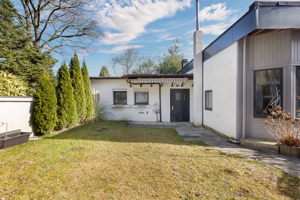 Garten mit Rasenfläche und Terrasse vor einem weißen Wohnhaus mit großen Fenstern.