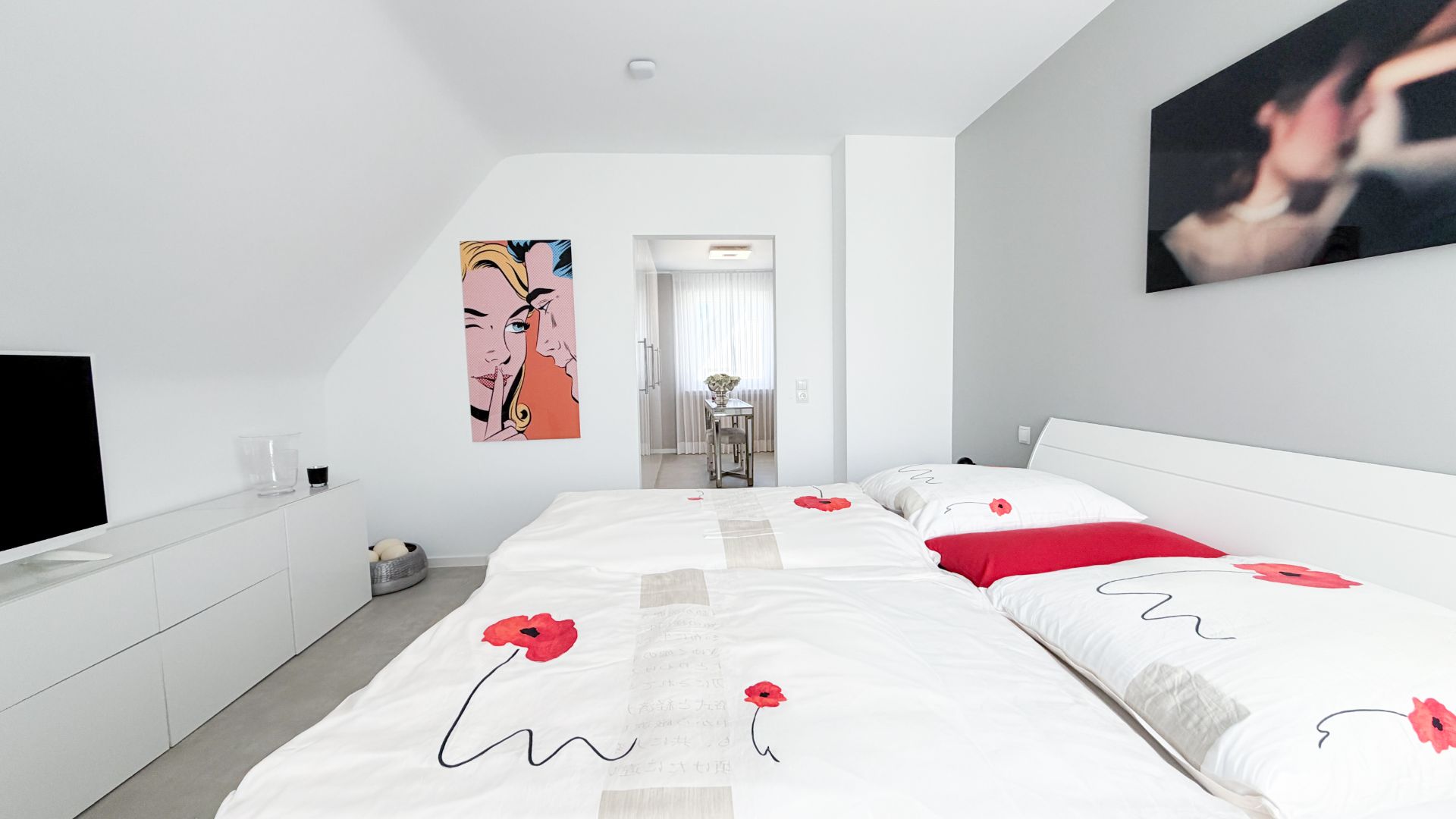 Helles Schlafzimmer mit Doppelbett, weißen Möbeln und bunter Wandkunst.
