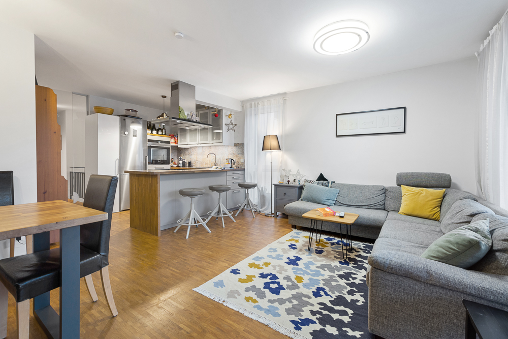 Modernes Wohnzimmer mit Ecksofa, Teppich, Esstisch und offener Küche mit Tresen.