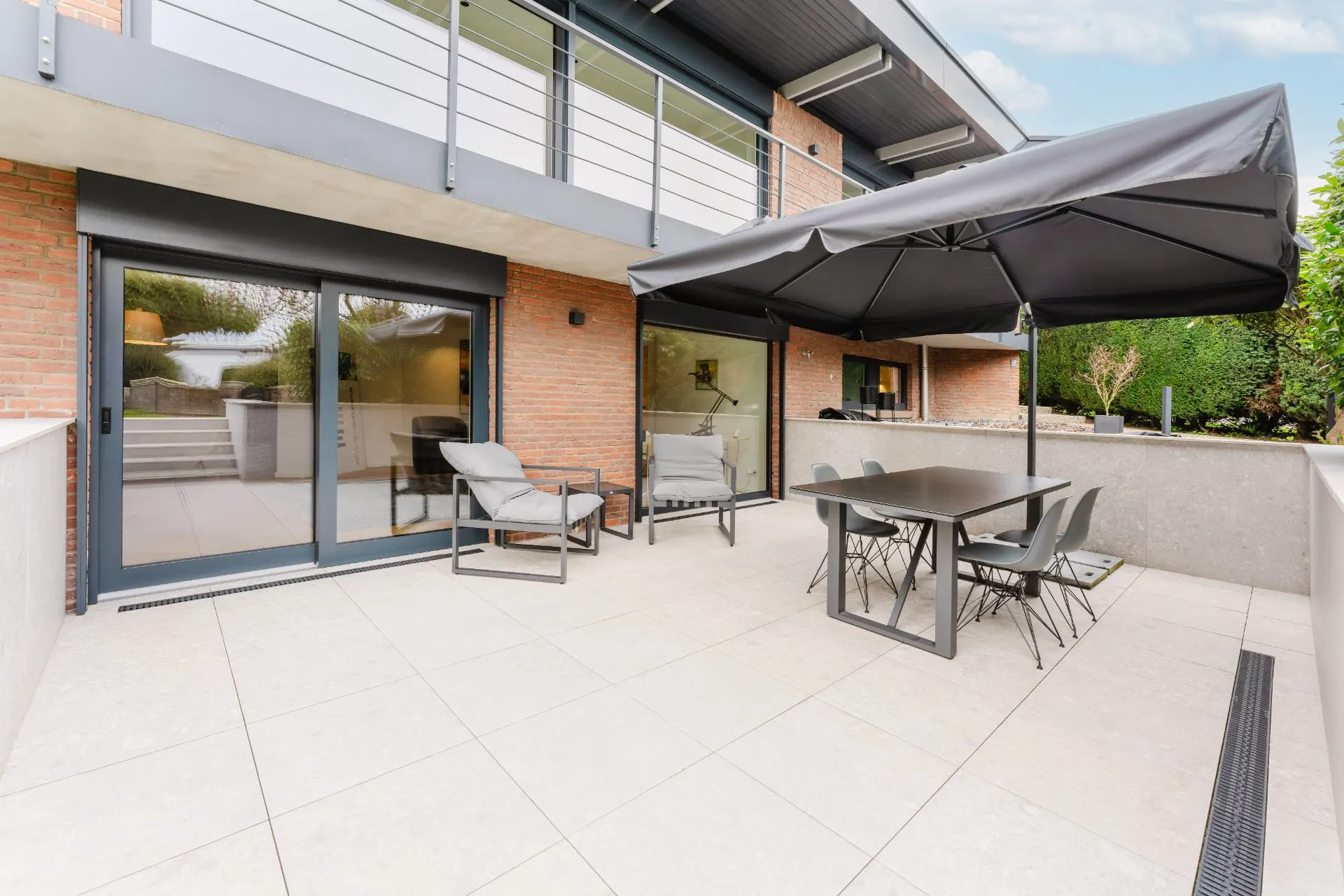 Moderne Terrasse mit Tisch, Stühlen, Sonnenschirm und Liegestuhl vor einem Haus.
