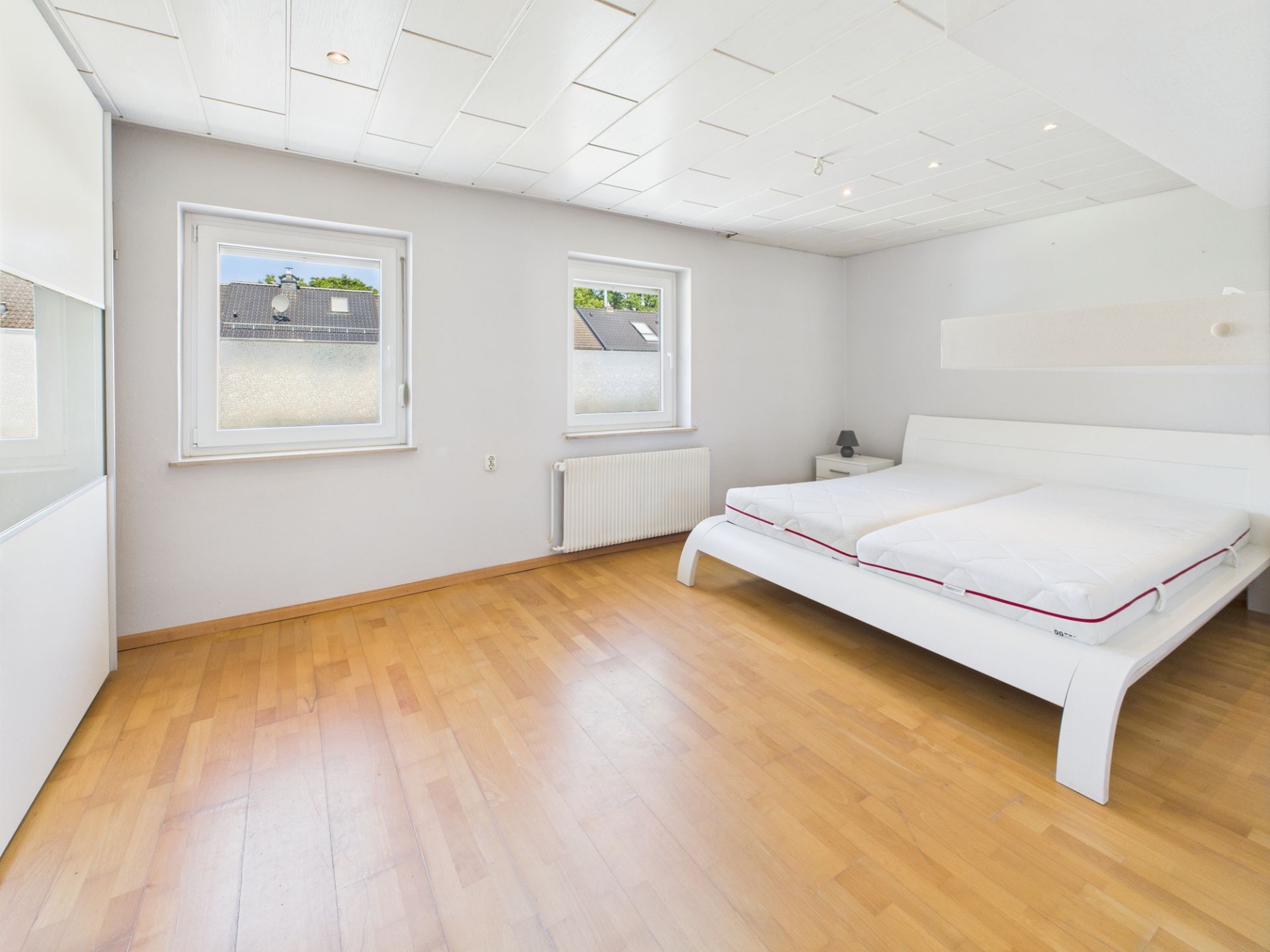 Helles Schlafzimmer mit Holzboden, Doppelbett und zwei Fenstern.