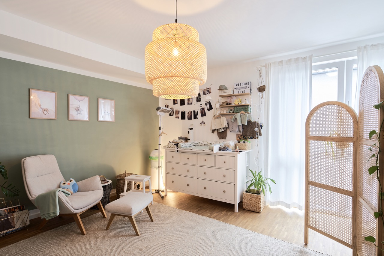 Helles Kinderzimmer mit Sessel, Wickelkommode und Spielzeug-Eule, große Lampe an der Decke.