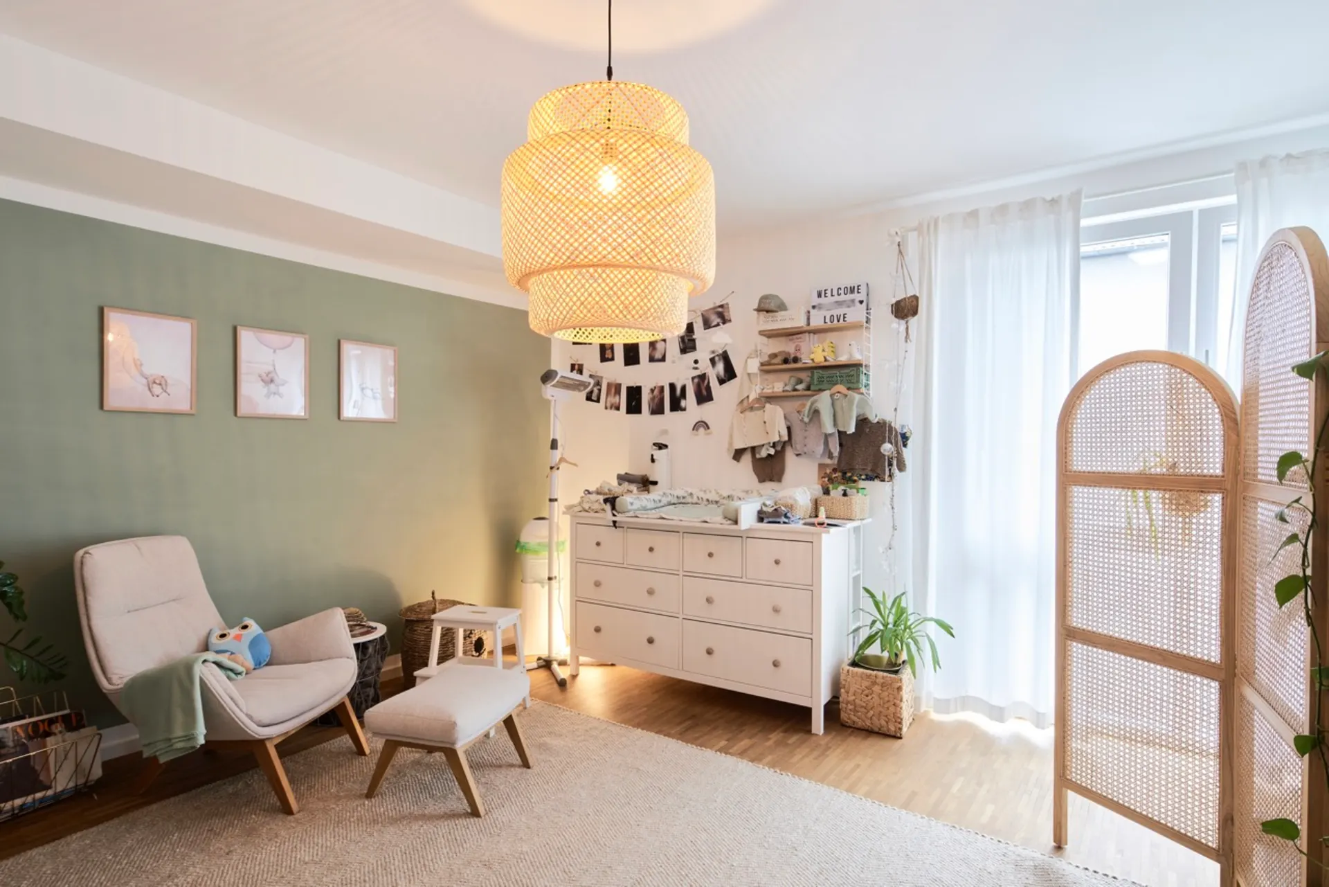 Helles Kinderzimmer mit Sessel, Wickelkommode und Spielzeug-Eule, große Lampe an der Decke.