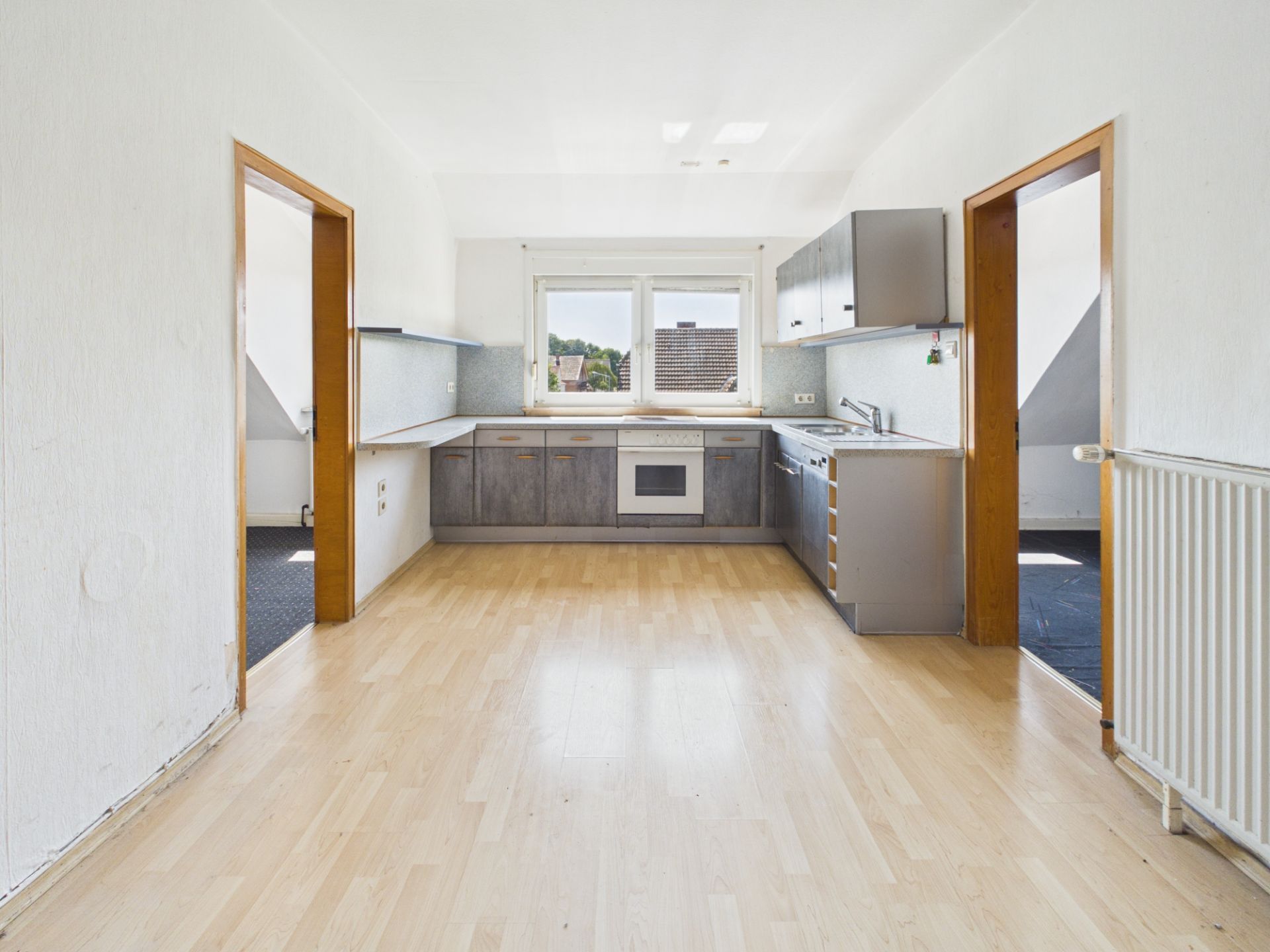 Helle Einbauküche mit Holzfußboden, Fenster und zwei offenen Türen zu Nebenräumen.