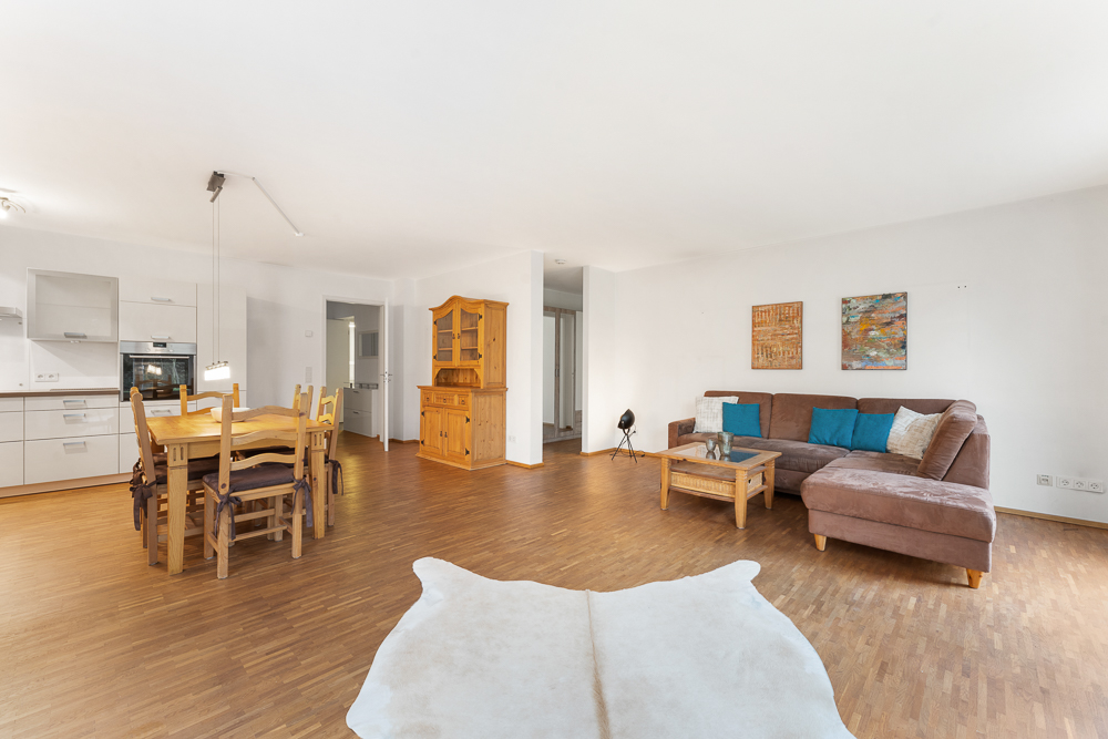 Helles Wohnzimmer mit Ecksofa, Couchtisch, Esstisch, Holzmöbeln und offener Küche.