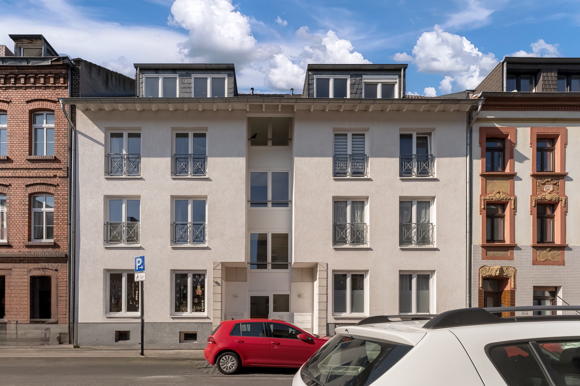 Vorderansicht eines mehrstöckigen Wohnhauses mit geparkten Autos davor.