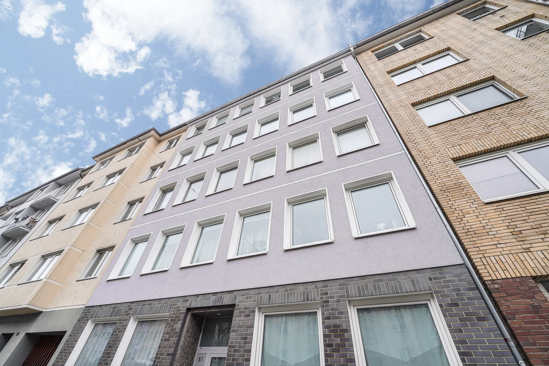 Vorderansicht eines mehrstöckigen Wohngebäudes mit vielen Fenstern und lila Fassade.