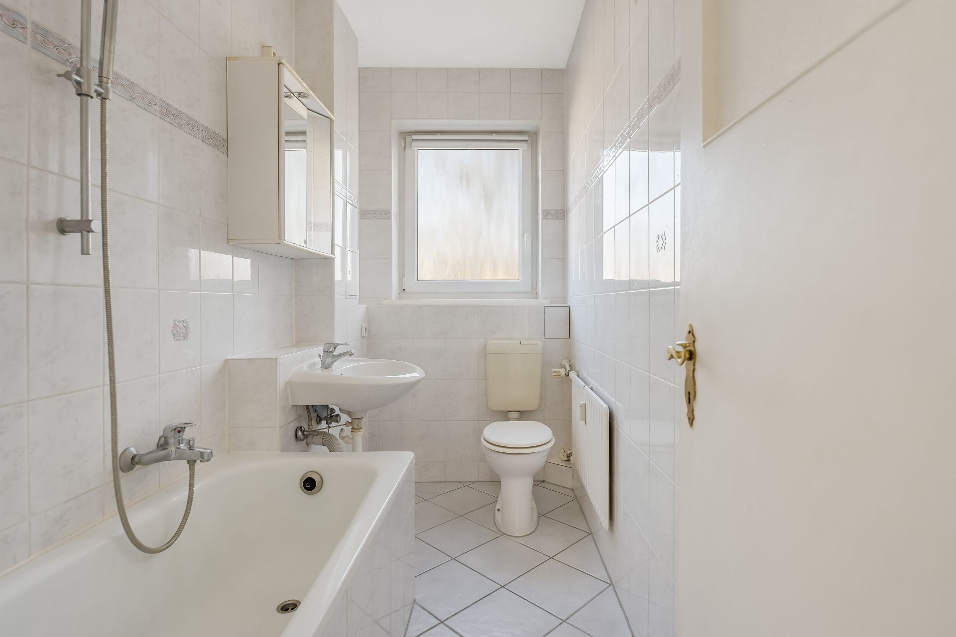 Helles Badezimmer mit Badewanne, Waschbecken, Spiegel, Toilette und Fenster.