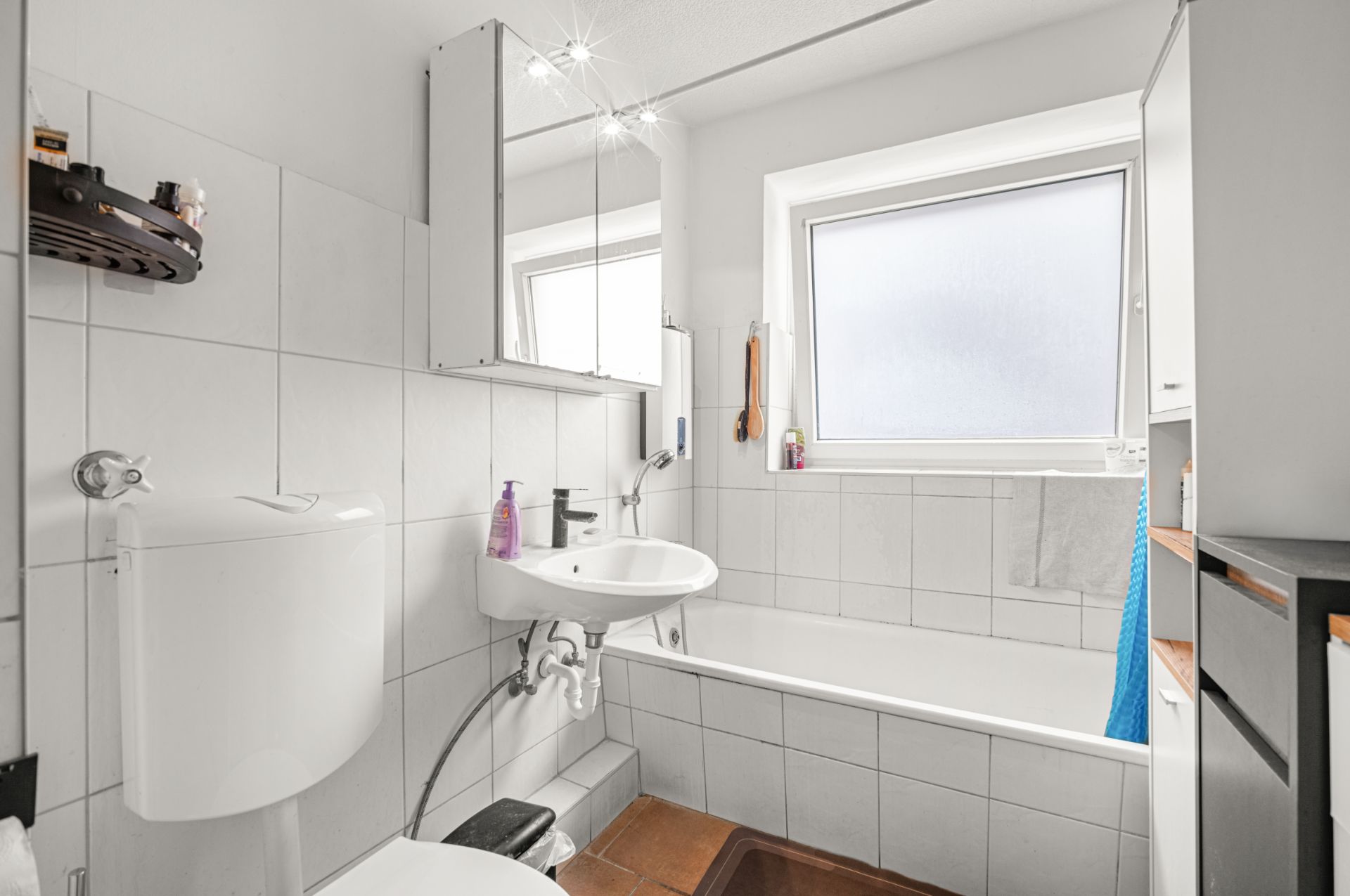 Helles Badezimmer mit Badewanne, Waschbecken, Spiegel und Fenster.