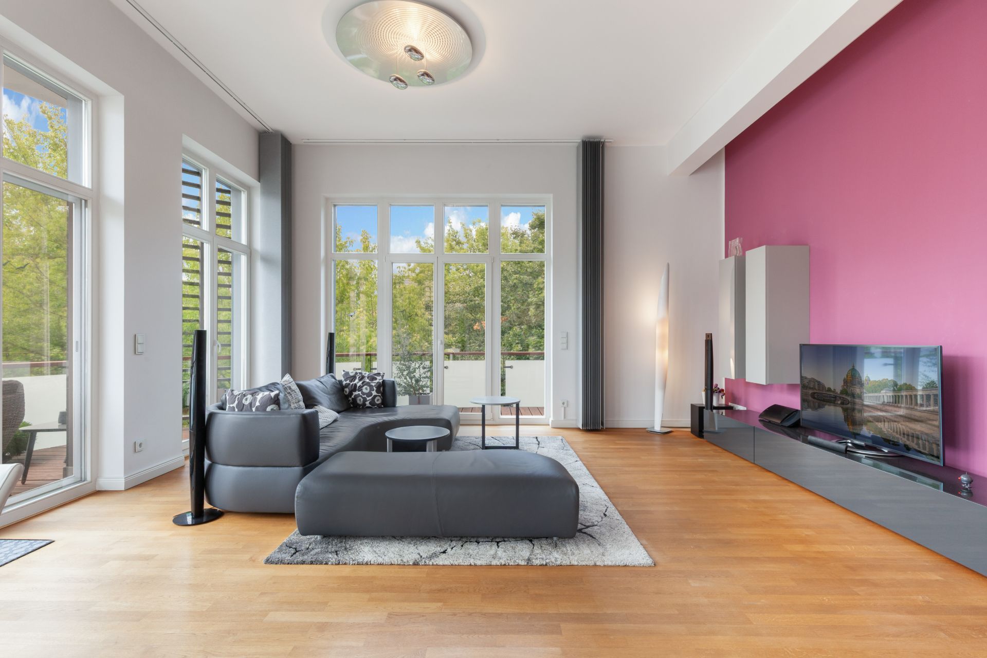 Modernes Wohnzimmer mit grauem Ecksofa, Teppich, Fernseher und großer Fensterfront.