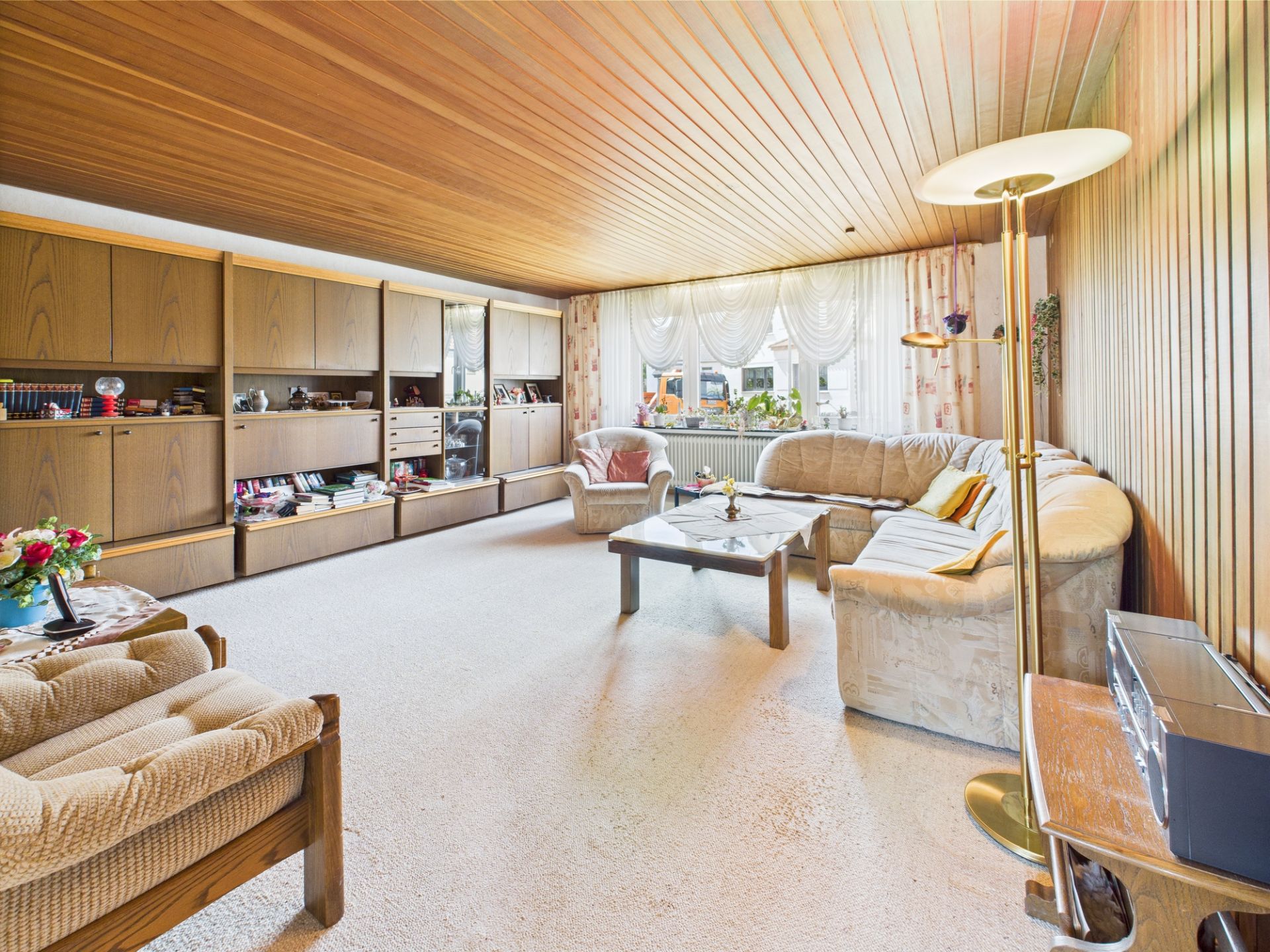 Gemütliches Wohnzimmer mit Holzdecke, Ecksofa, Sessel, Couchtisch und Regalwand.