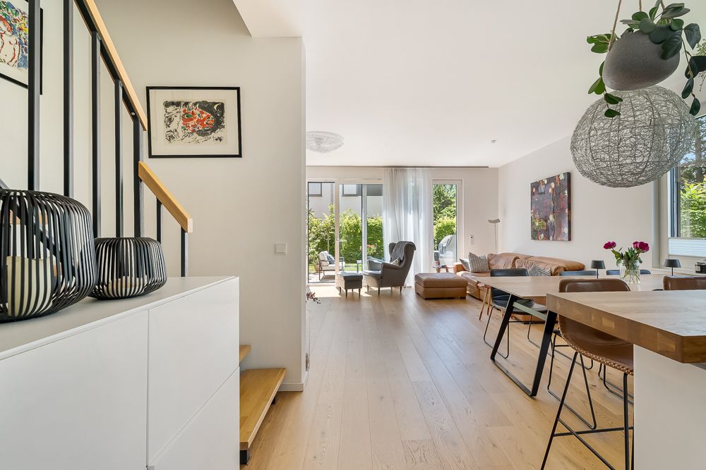 Modernes Wohnzimmer mit Holzfußboden, Essbereich und großen Fenstern zum Garten.