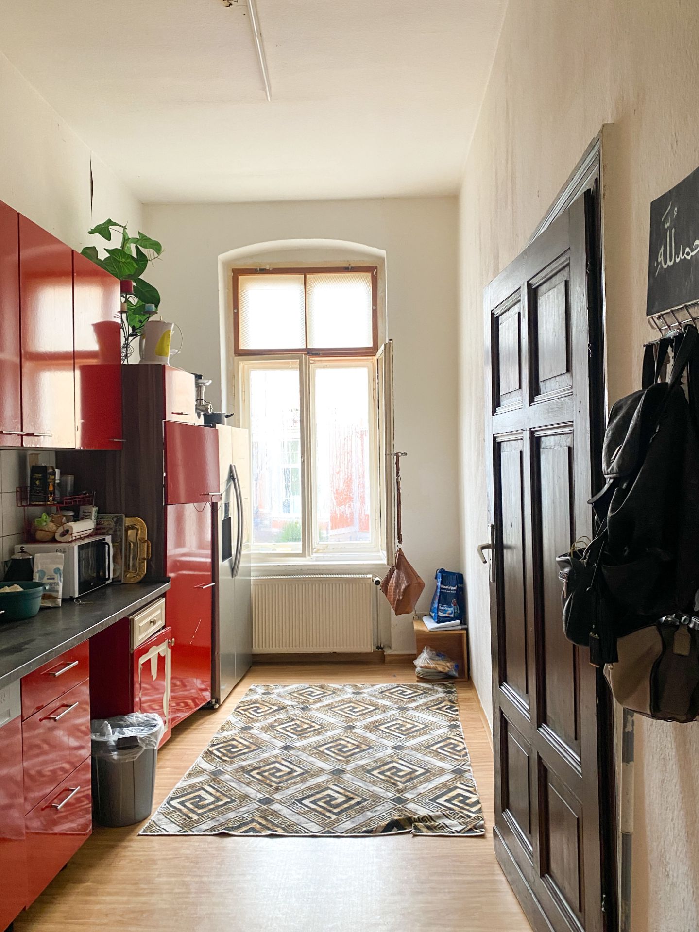 Helle Küche mit roten Schränken, großem Fenster und gemustertem Teppich auf Holzboden.