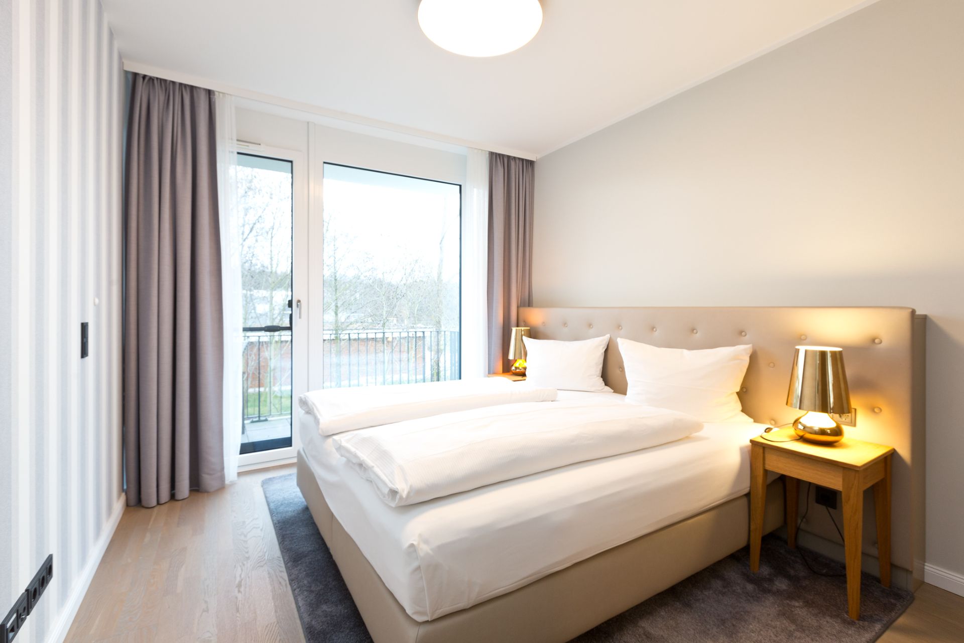 Helles Schlafzimmer mit großem Bett, zwei Nachttischen und Fenstertür zum Balkon.