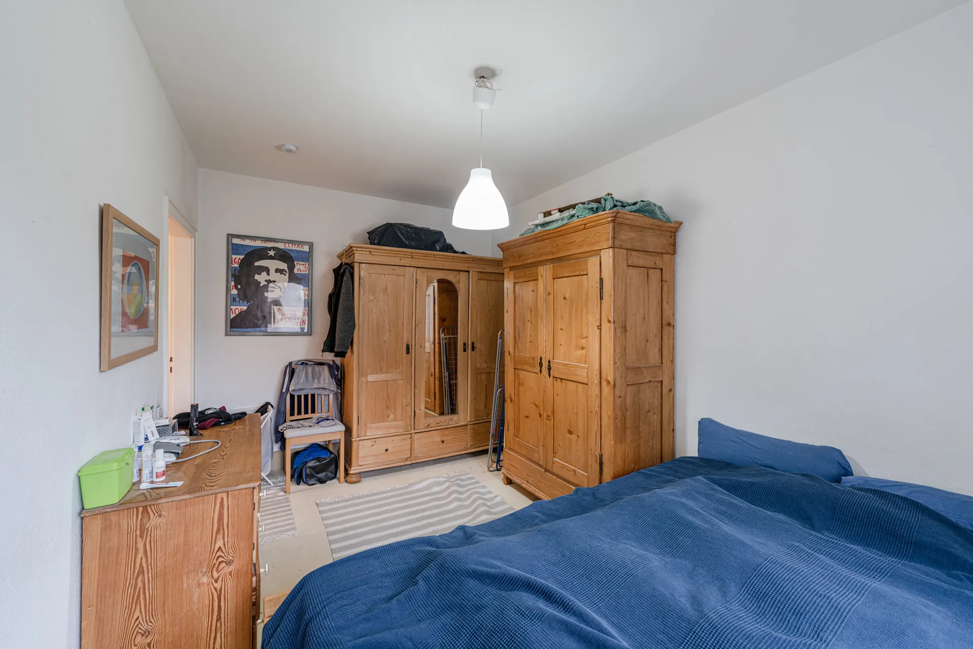 Schlafzimmer mit Holzbett, Kommode, zwei Kleiderschränken und blauer Bettdecke.