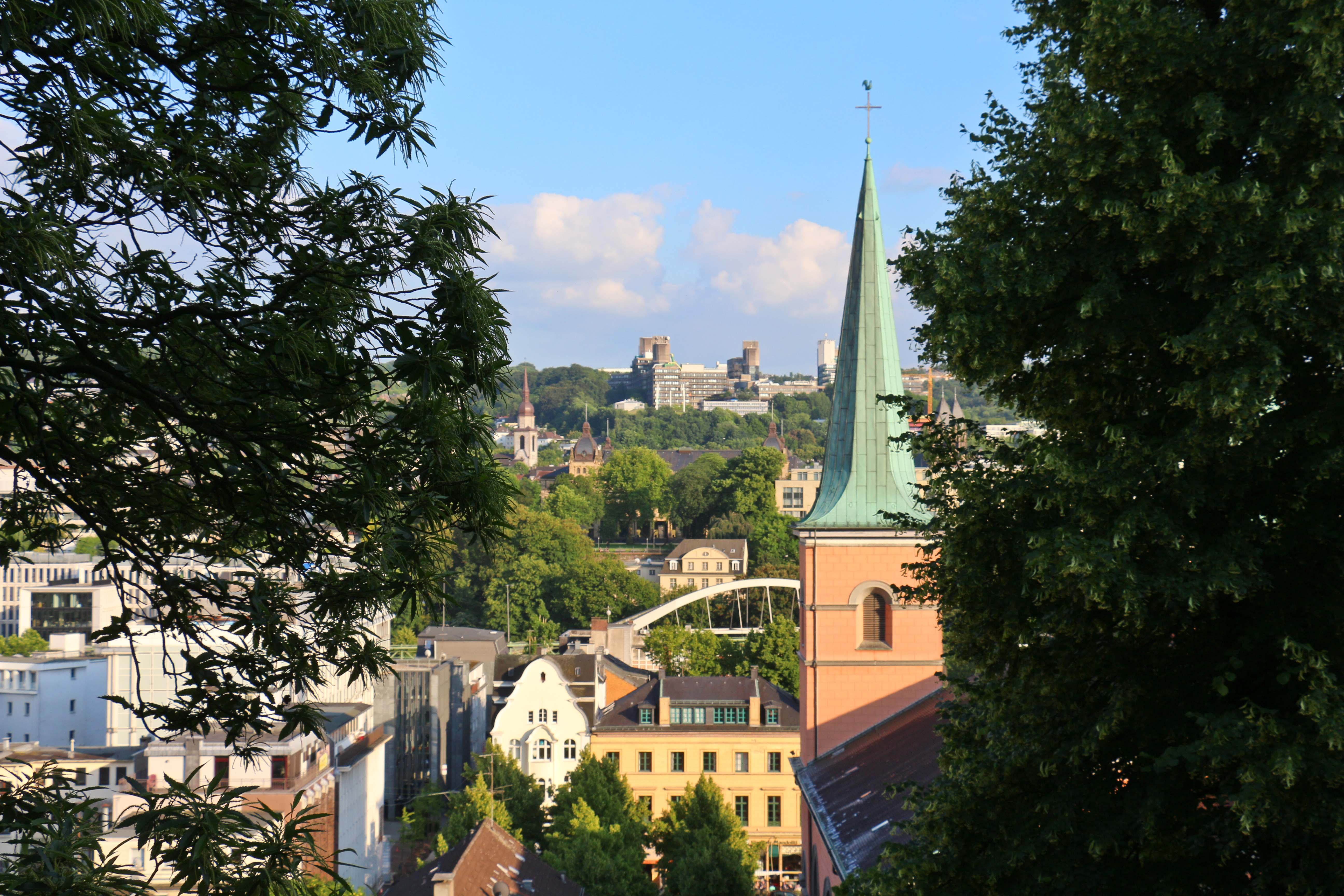Blick auf eine Stadt mit Kirche, Bäumen und Gebäuden im Sonnenschein.