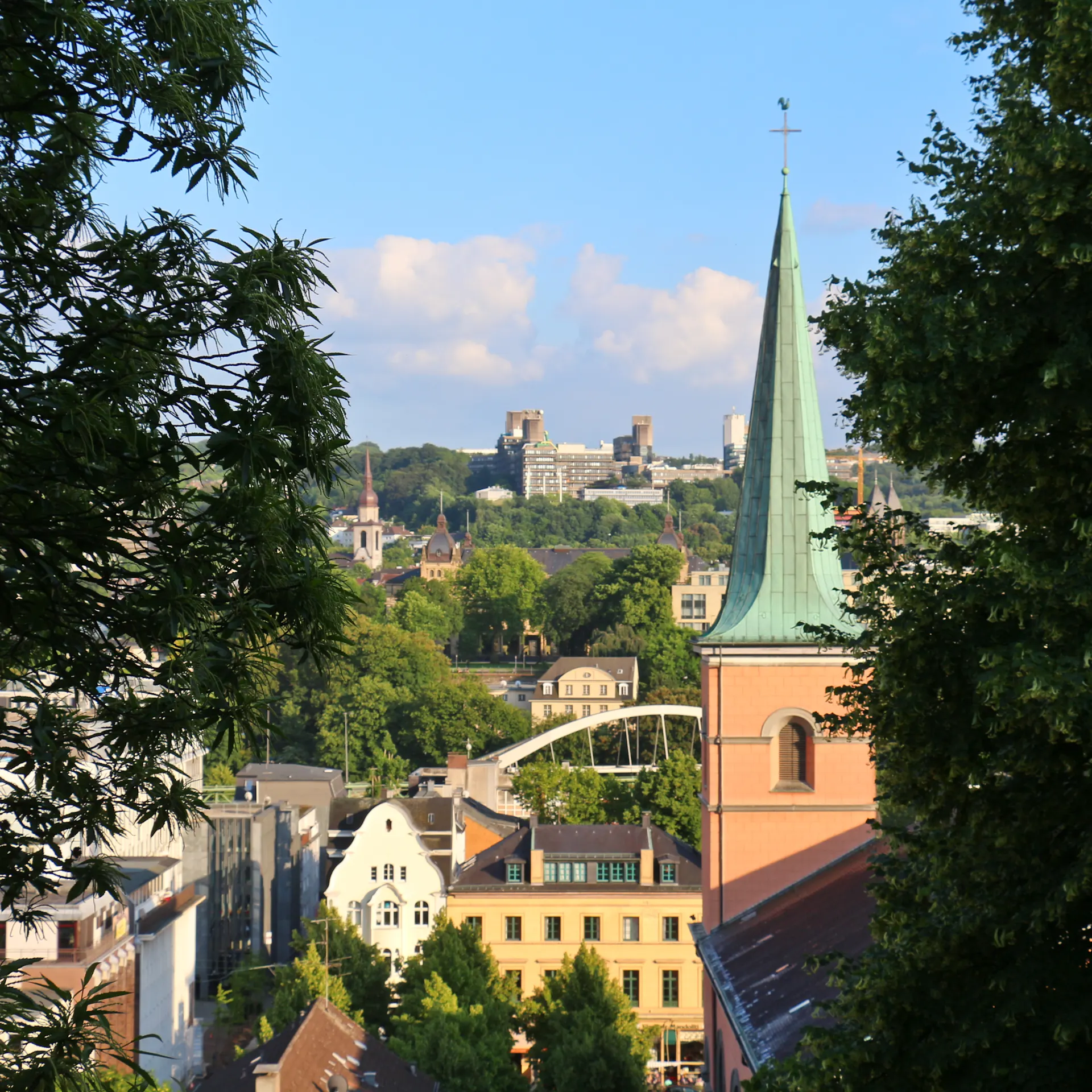 Blick auf eine Stadt mit Kirche, Bäumen und Gebäuden im Sonnenschein.