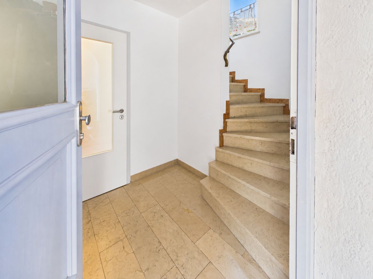 Eingangsbereich mit gefliestem Boden, einer Tür links und einer Treppe nach oben.