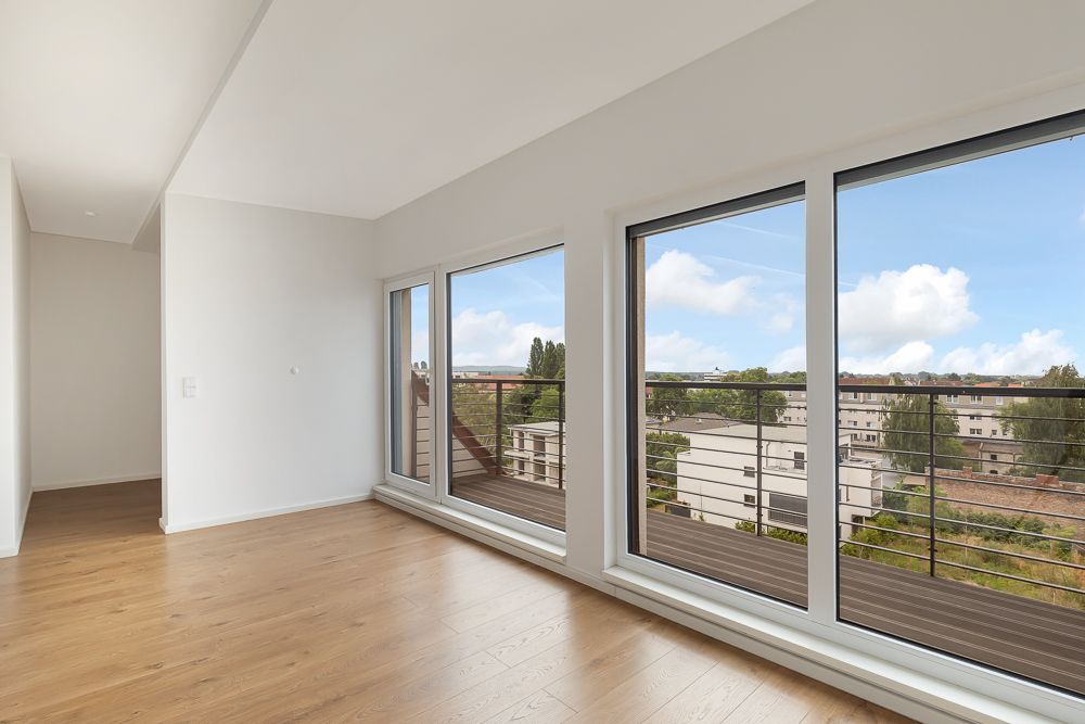 Heller Raum mit Holzboden und großen Fenstern mit Blick auf Stadt und Balkon.