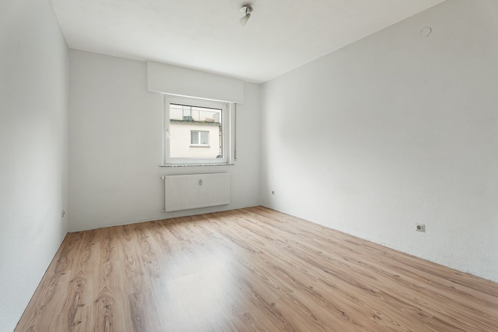 Leerer Raum mit weiß gestrichenen Wänden, Fenster, Heizkörper und Laminatboden.