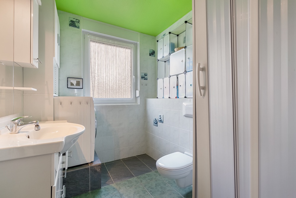 Modernes Badezimmer mit grünem Dach, Waschbecken, Waschmaschine, Toilette und Fenster.