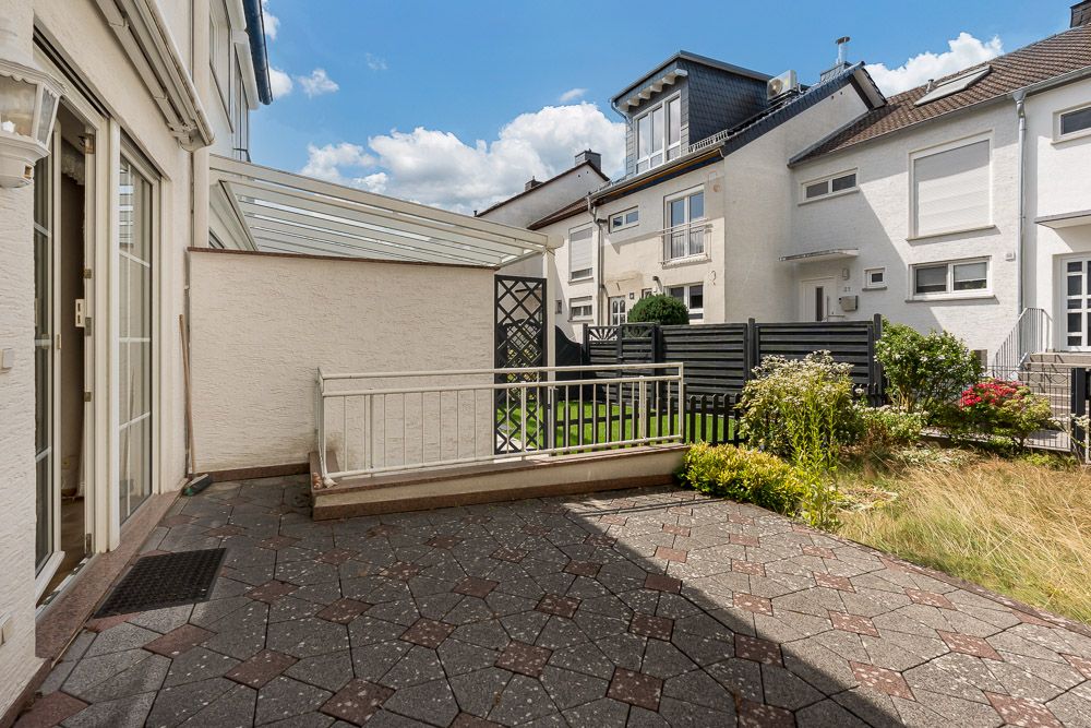 Gepflasterte Terrasse mit Geländer, kleiner Gartenbereich und Blick auf benachbarte Wohnhäuser.