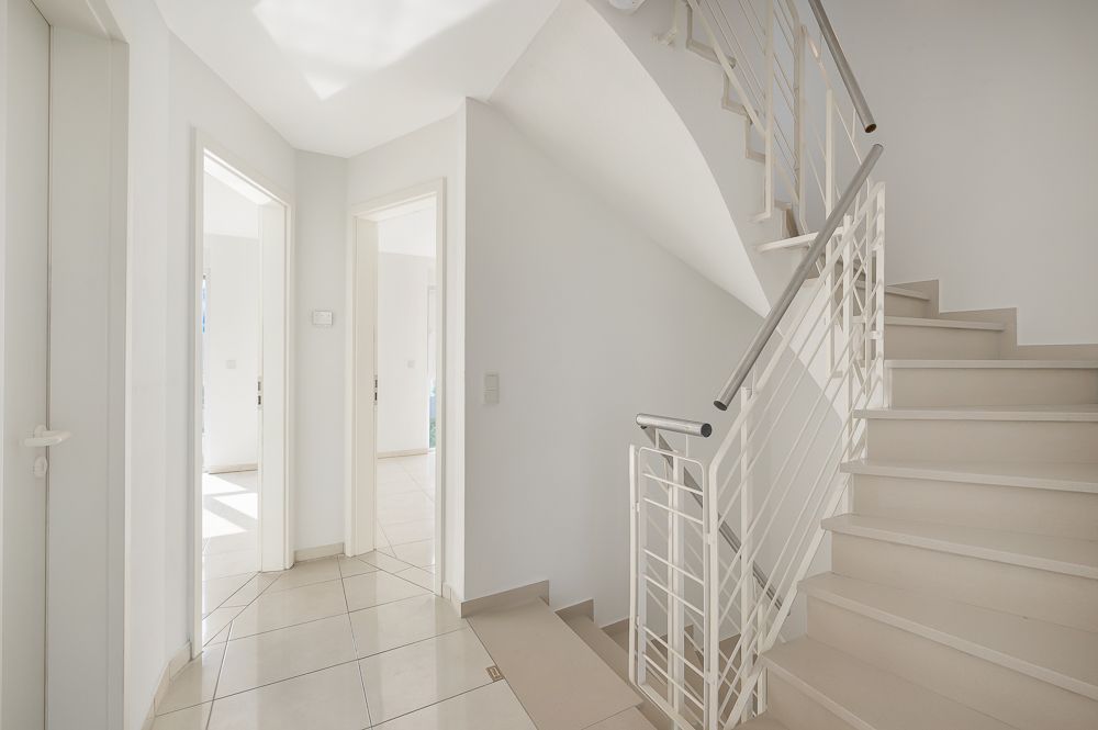 Heller Flur mit gefliesten Boden, zwei offenen Türen und einer Treppe mit weißem Geländer.
