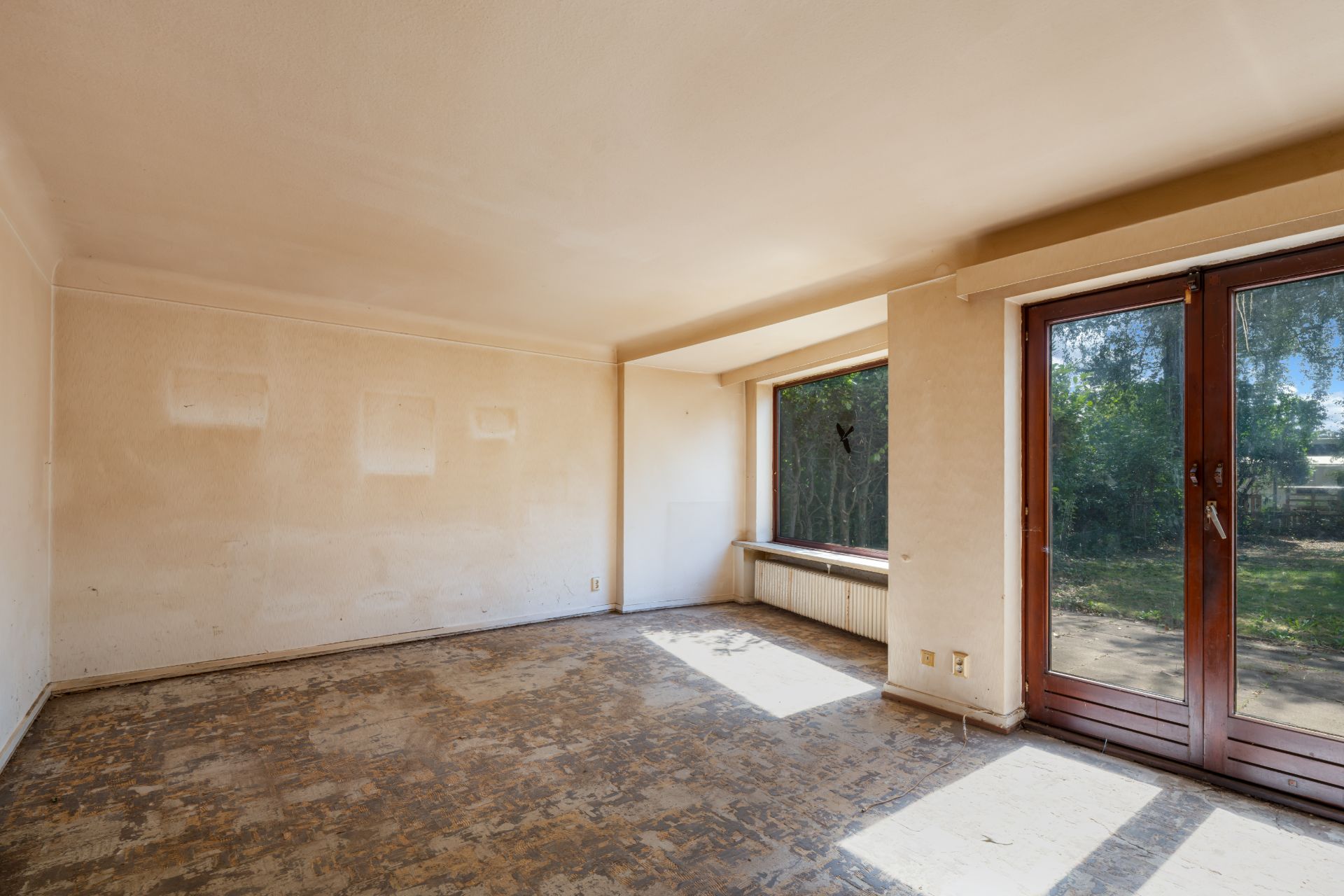 Leeres Zimmer mit großem Fenster und Glastür zum Garten, ohne Bodenbelag.