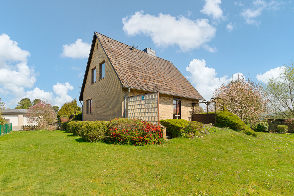 Einfamilienhaus aus Klinker mit Satteldach im Garten, umgeben von Büschen und Bäumen.