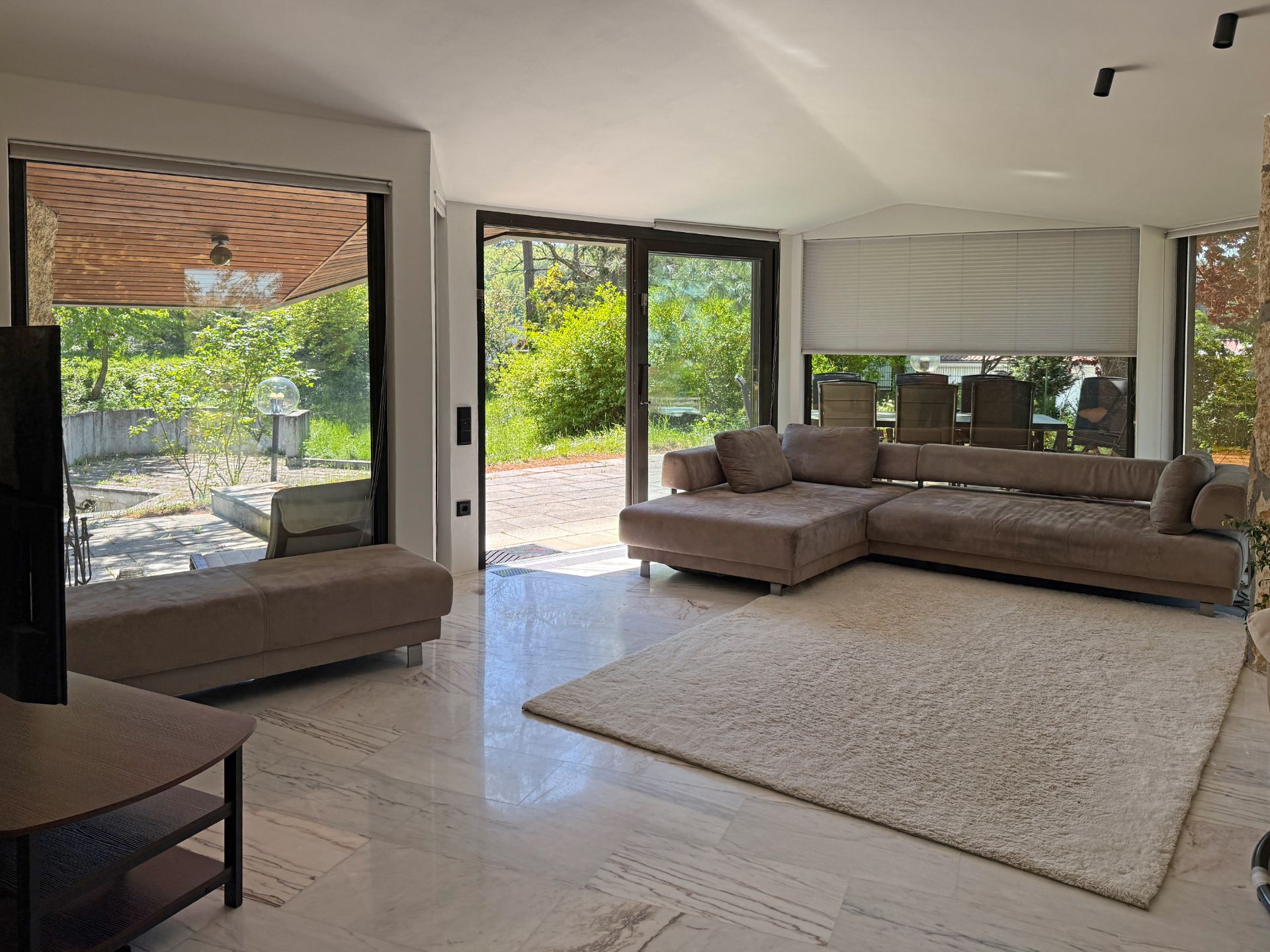 Helles Wohnzimmer mit großer Eckcouch, Teppich und Blick durch große Fenster auf den Garten.