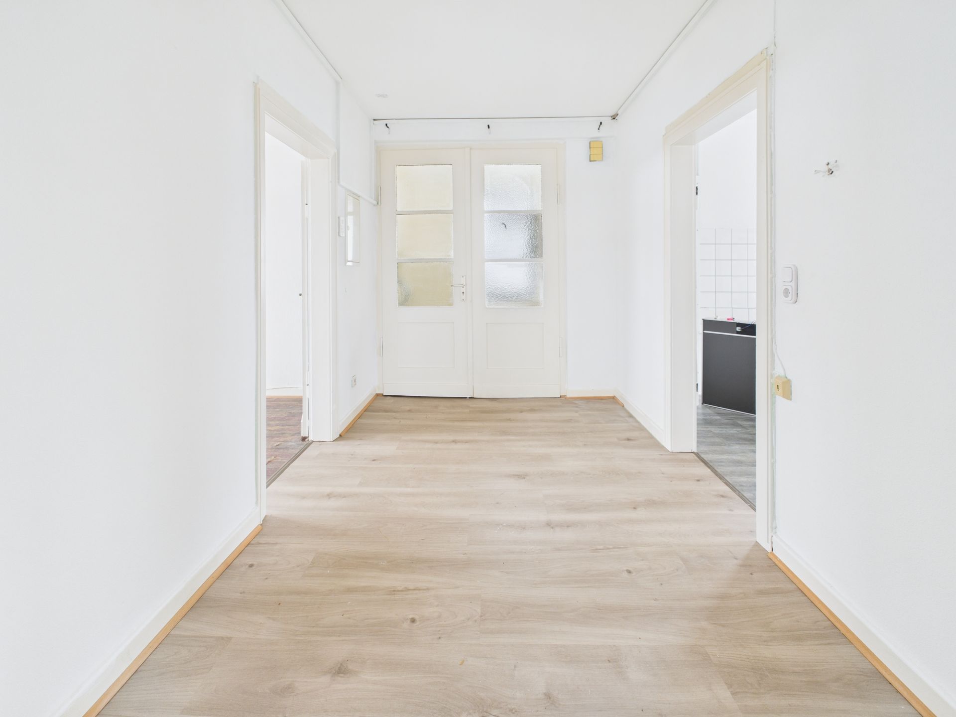 Heller Flur mit Holzboden, weißen Wänden und drei Türen in einer Wohnung.