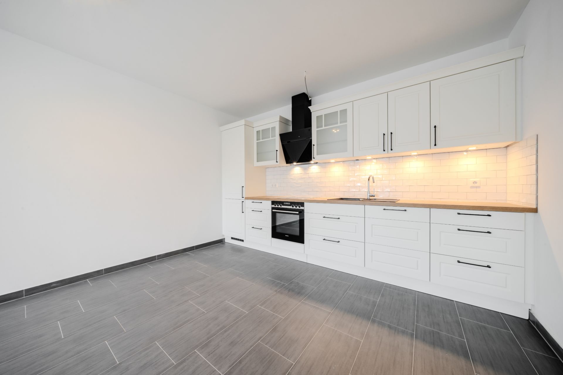 Moderne Einbauküche mit weißen Schränken und grauem Fliesenboden, leerer Raum.