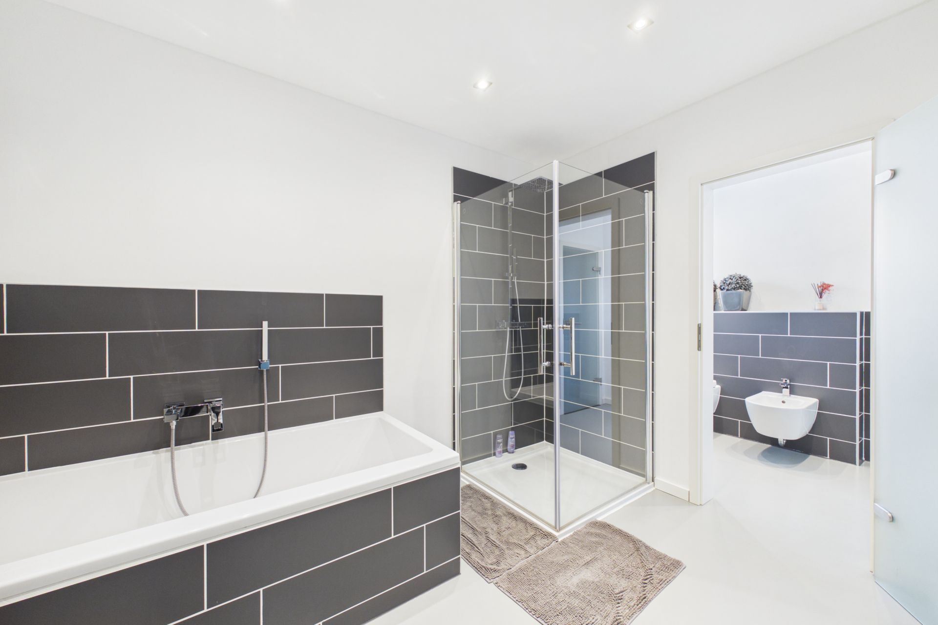 Modernes Badezimmer mit Badewanne, Dusche und Blick auf ein separates WC.
