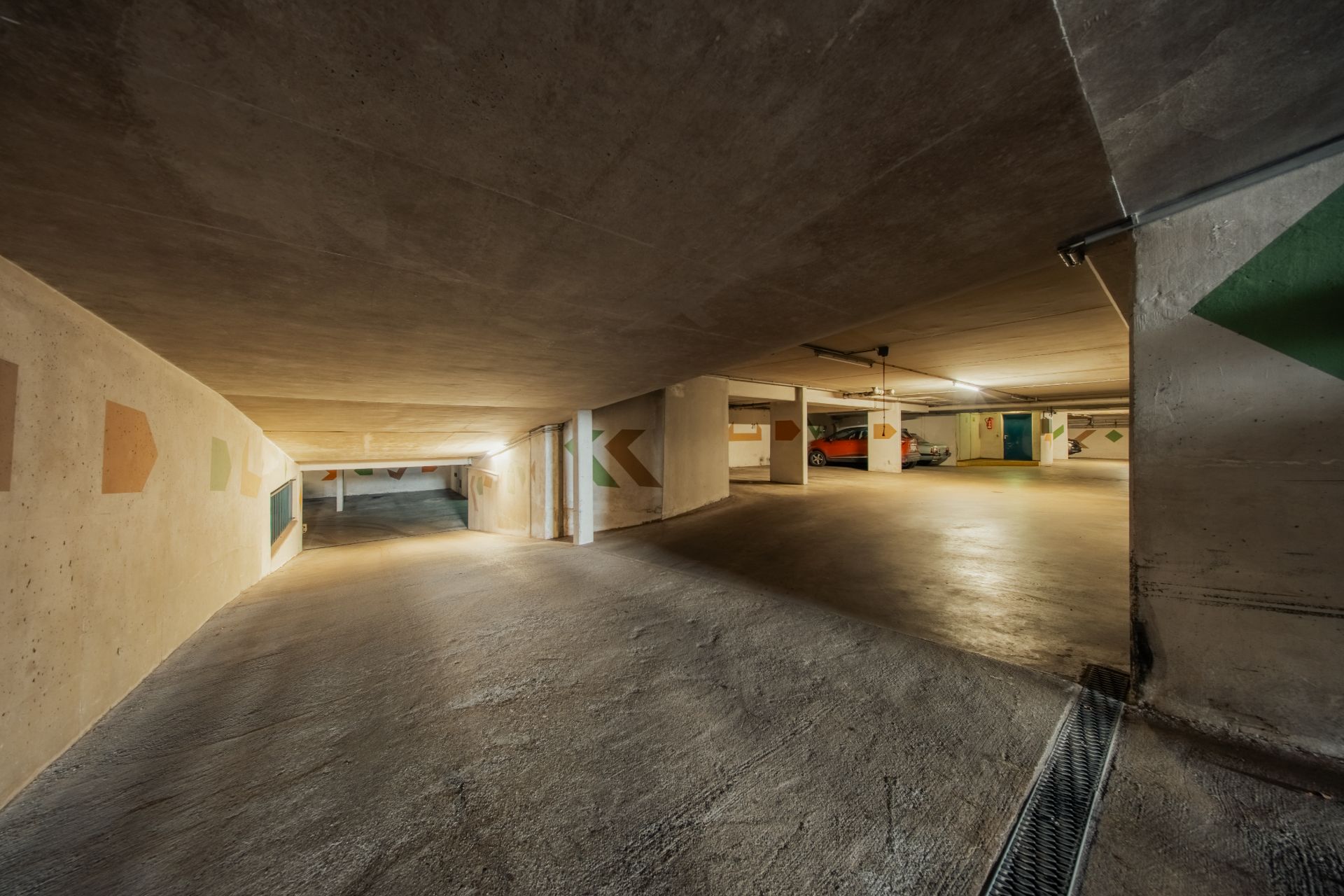 Unterirdische Tiefgarage mit mehreren Parkplätzen und Betonwänden mit Pfeilen.
