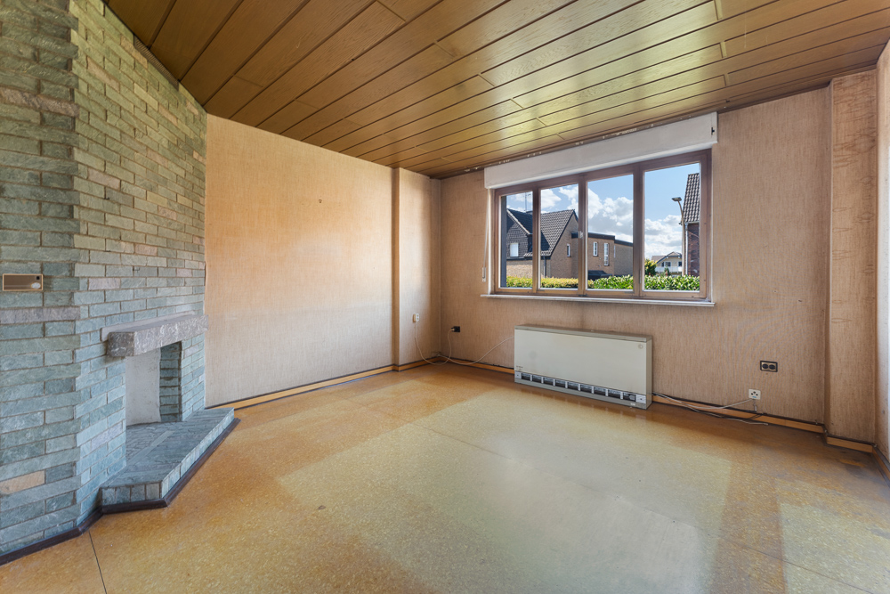 Leerer Raum mit Kamin, großem Fenster und Holzdecke in einem Wohnhaus.