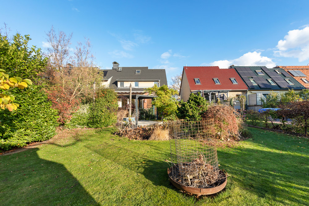 Grüner Garten mit Büschen vor Reihenhäusern an einem sonnigen Tag.