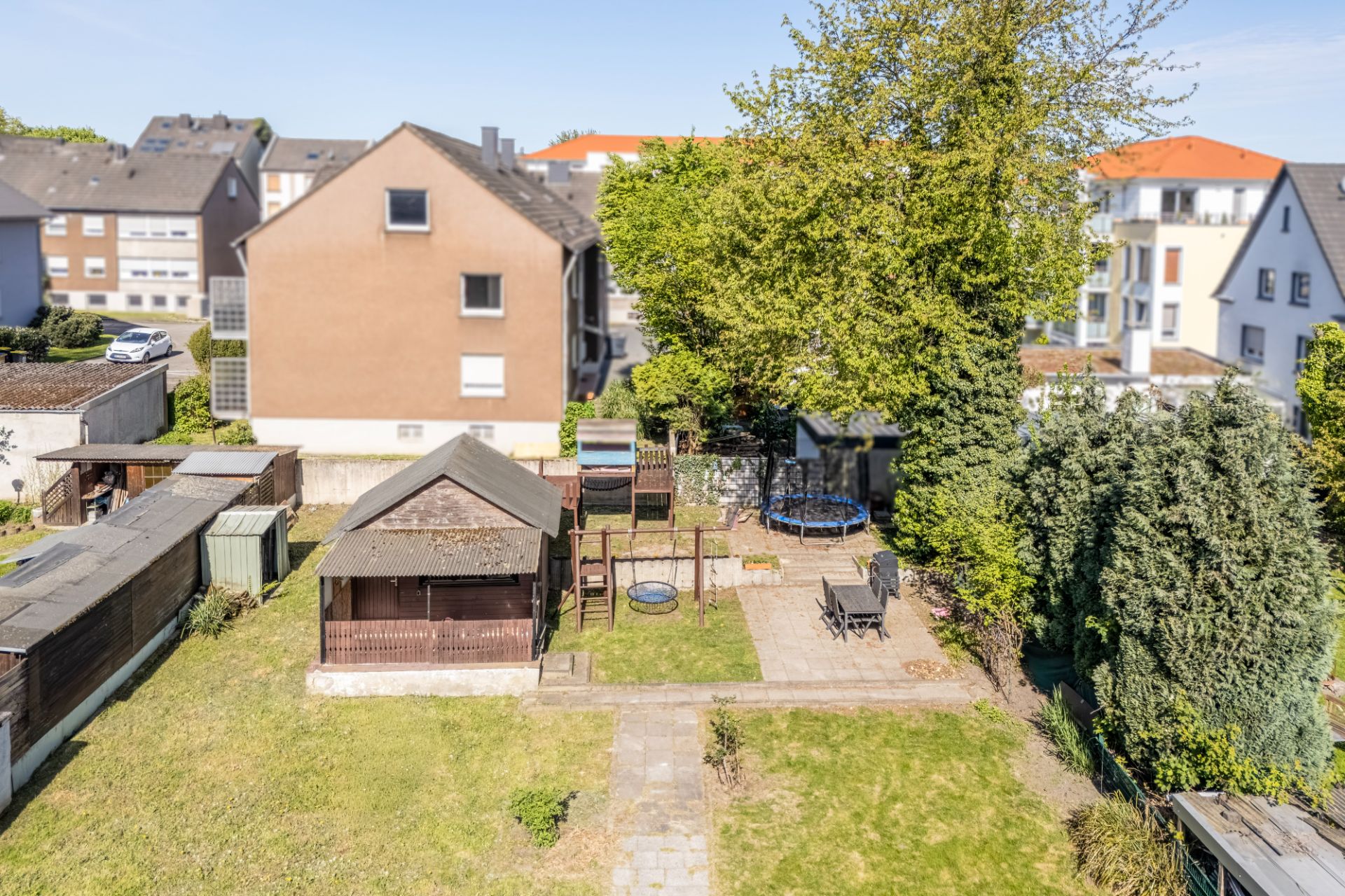 Garten mit Gartenhaus, Terrasse, Spielplatz und Bäumen, umgeben von Nachbarhäusern.