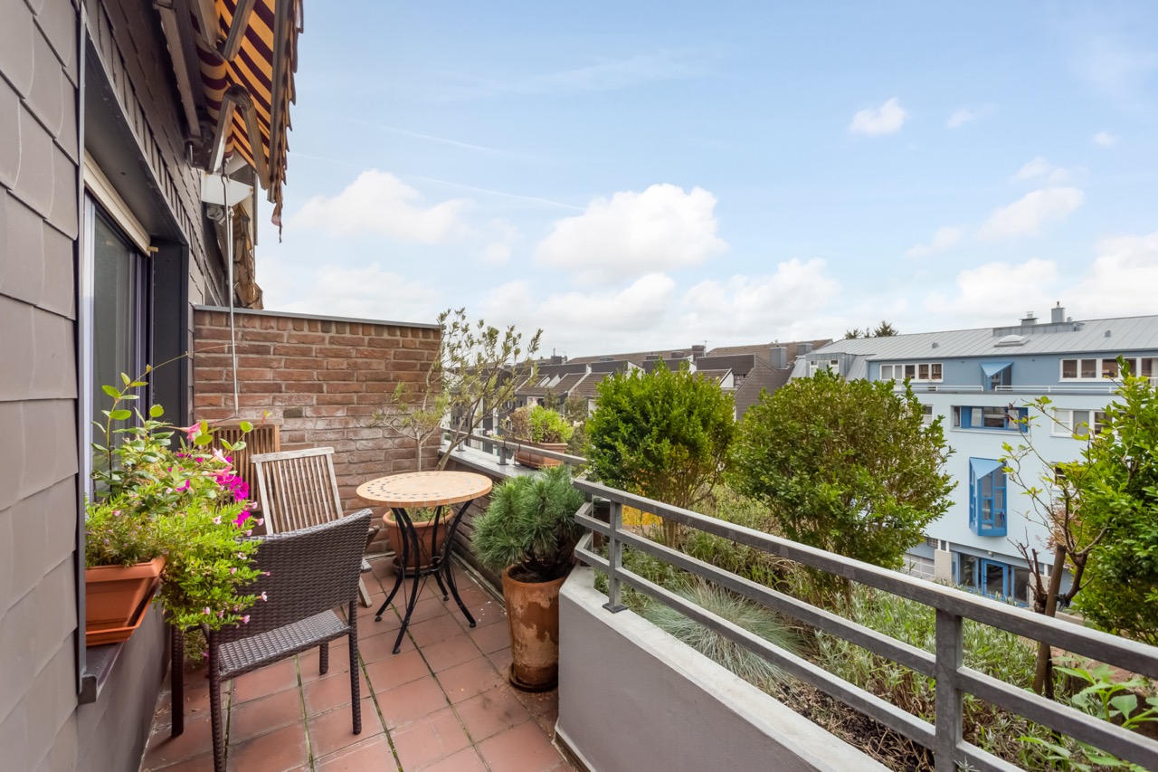 Kleiner Balkon mit Tisch, Stühlen und vielen Pflanzen, Blick auf Wohnhäuser.