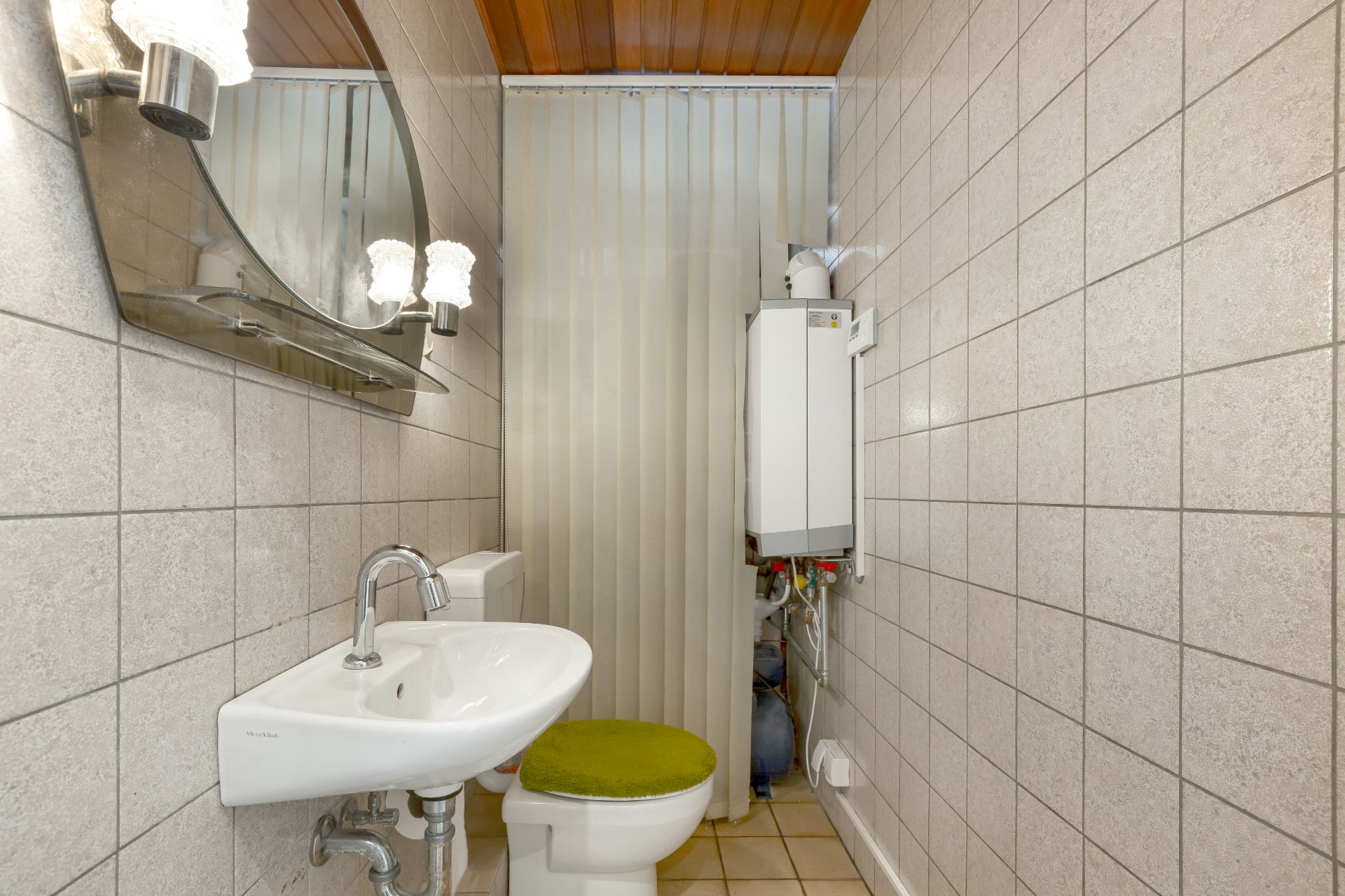 Schmales Badezimmer mit Waschbecken, WC mit grünem Sitz und Wandboiler.