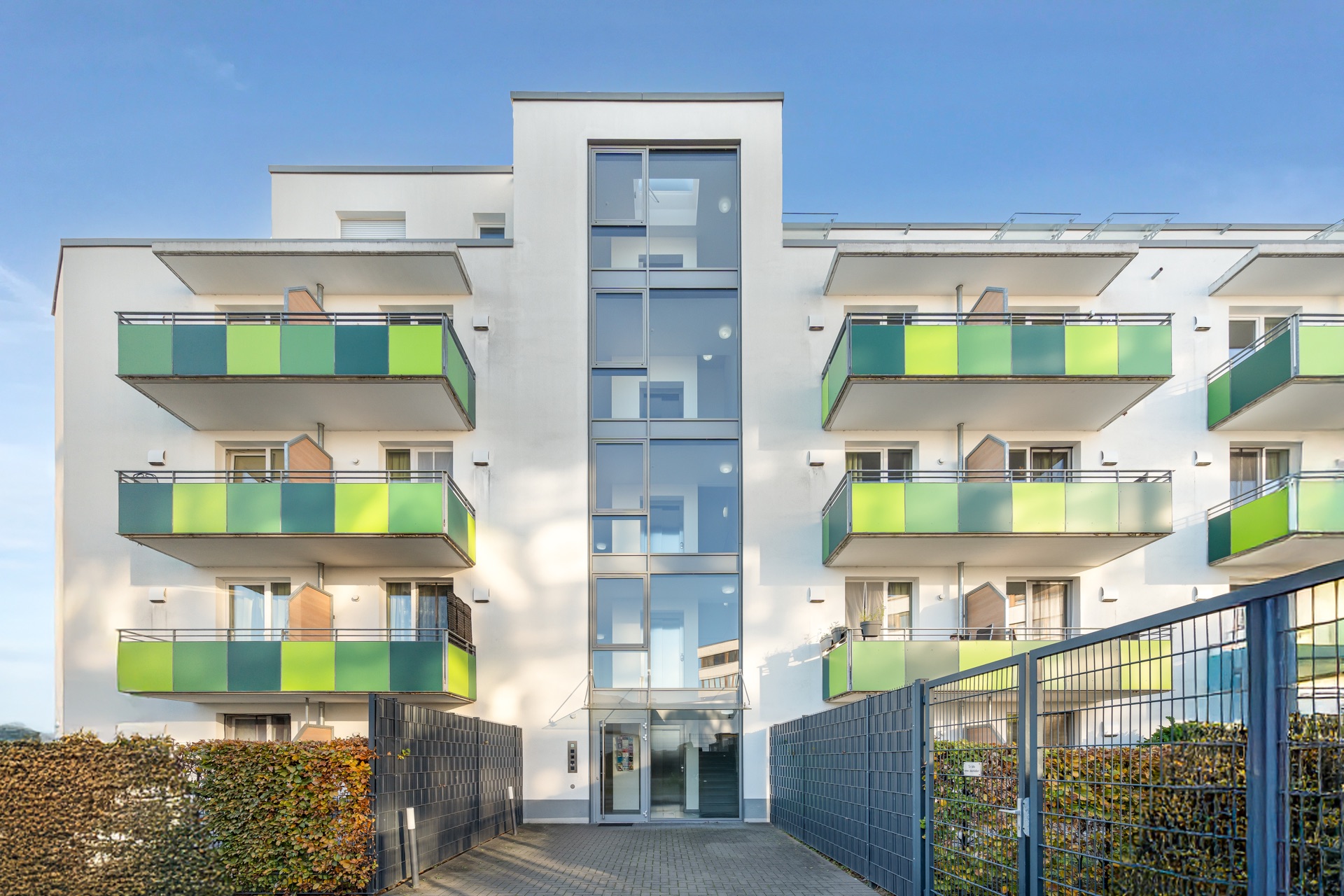 Modernes Wohngebäude mit grünen Balkonen und Glasfassade am Eingang.