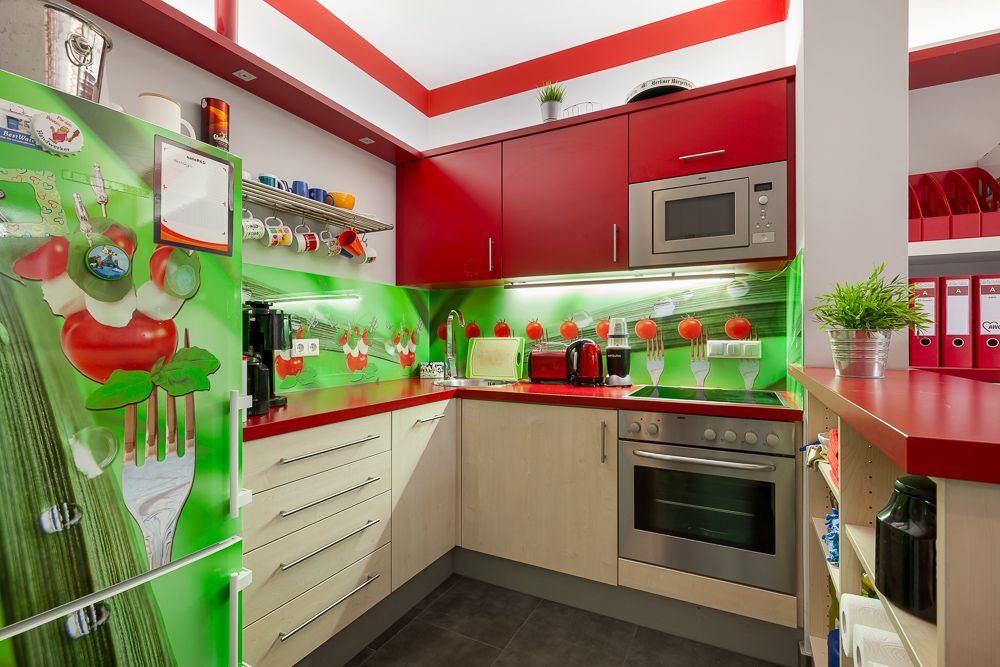 Moderne Küche mit roten Schränken, grünem Kühlschrank und Wanddekor mit Gemüse-Motiv.
