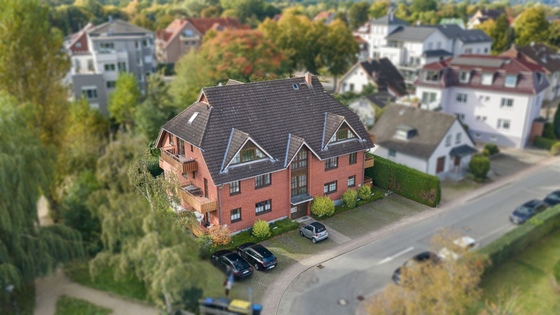 Backsteinhaus mit Satteldach, Balkonen und geparkten Autos vor dem Gebäude in Wohngegend.
