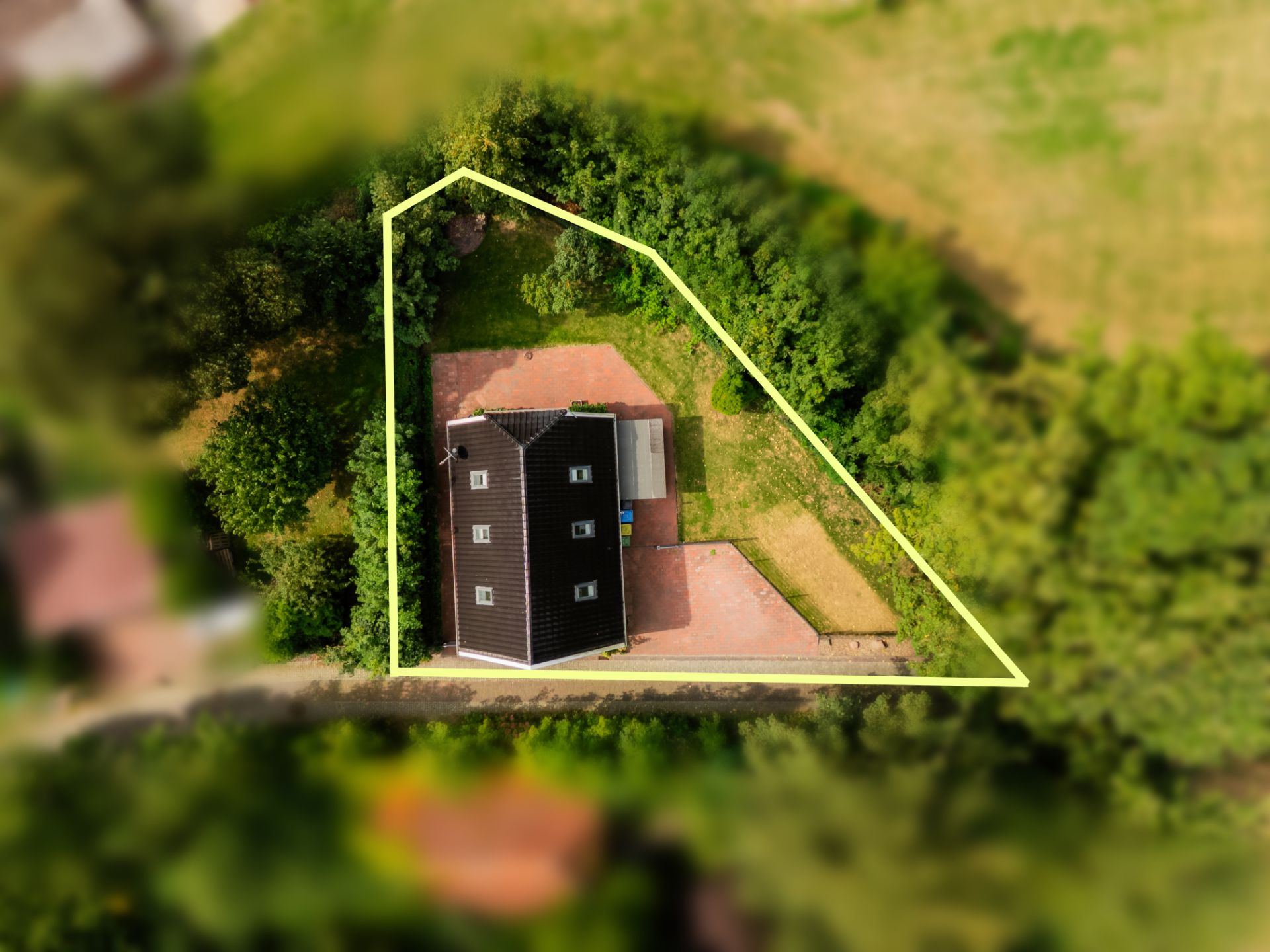 Luftaufnahme eines Hauses mit eingezäuntem Grundstück und umgebendem Grün.