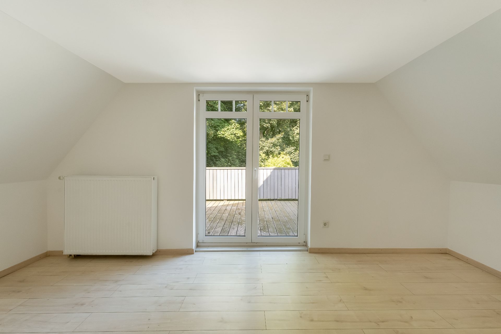 Leerer Raum mit Holzfußboden, Heizung und Glastür zu einer Terrasse.