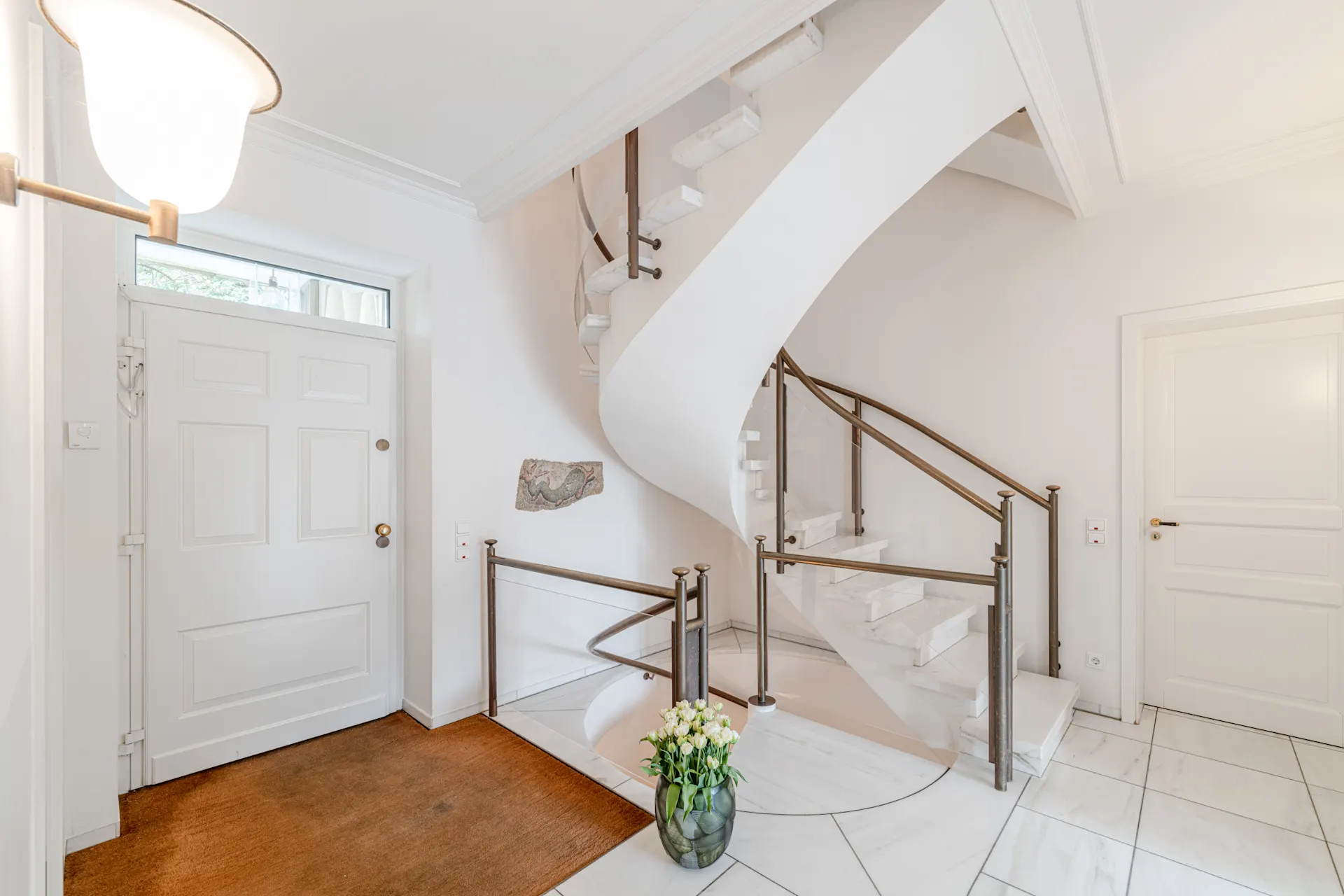Heller Flur mit weißer Haustür, Marmortreppe und Vase mit Blumen.