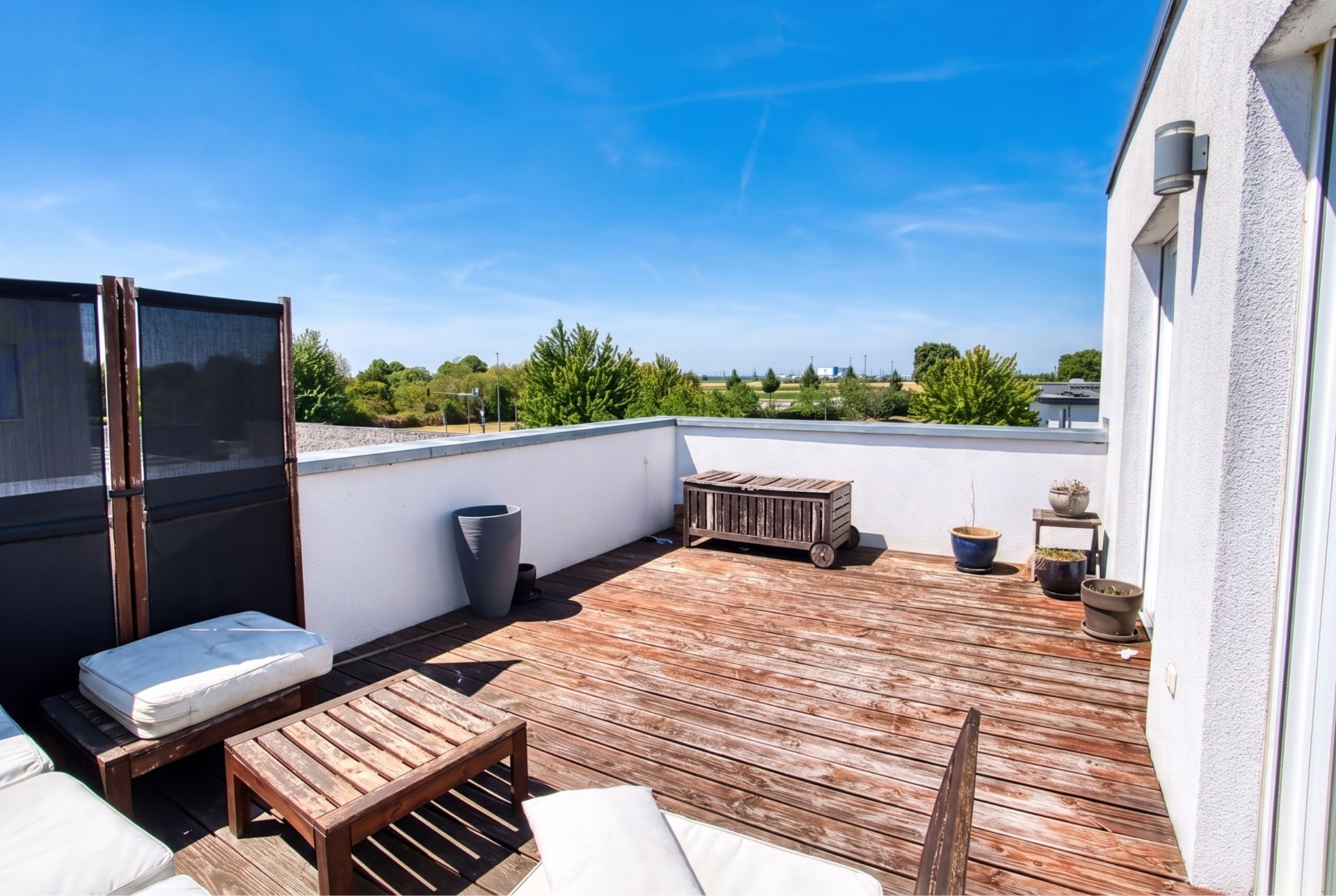Große Dachterrasse mit Holzboden, Sitzmöbeln und Pflanzkübeln, umgeben von weißer Brüstung.