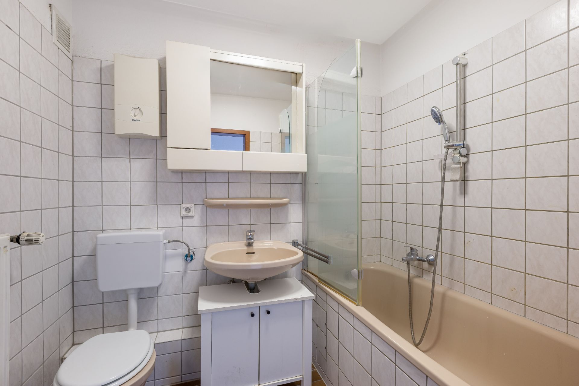 Kleines Badezimmer mit Badewanne, Dusche, Waschbecken, Spiegel und Toilette.