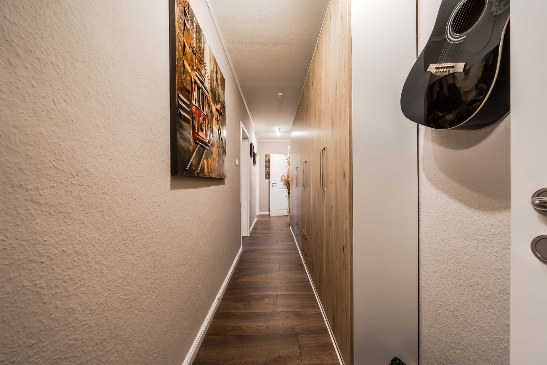Langer Flur mit Holzboden, Schränken, Wandbild und einer Gitarre an der Wand.